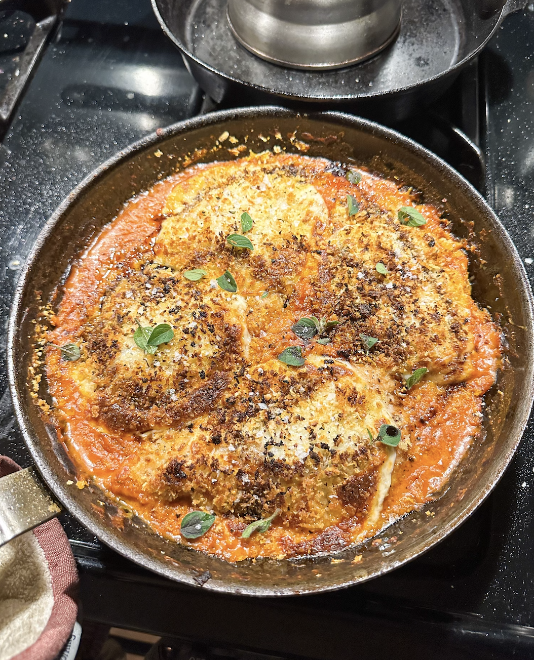 Chicken Parm covered in cheese and bread crumbs in a skillet
