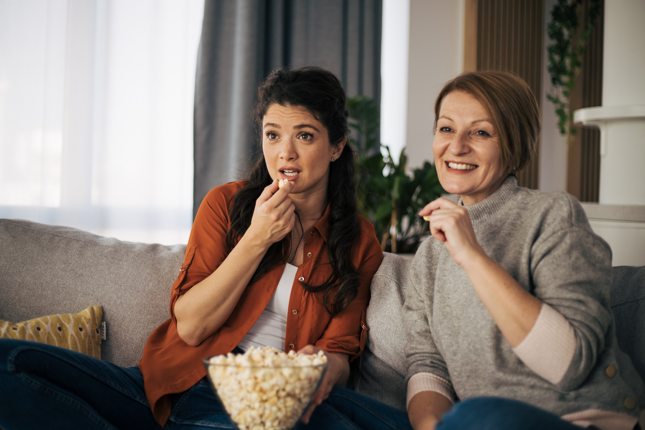 two women eating popcorn and watching TV