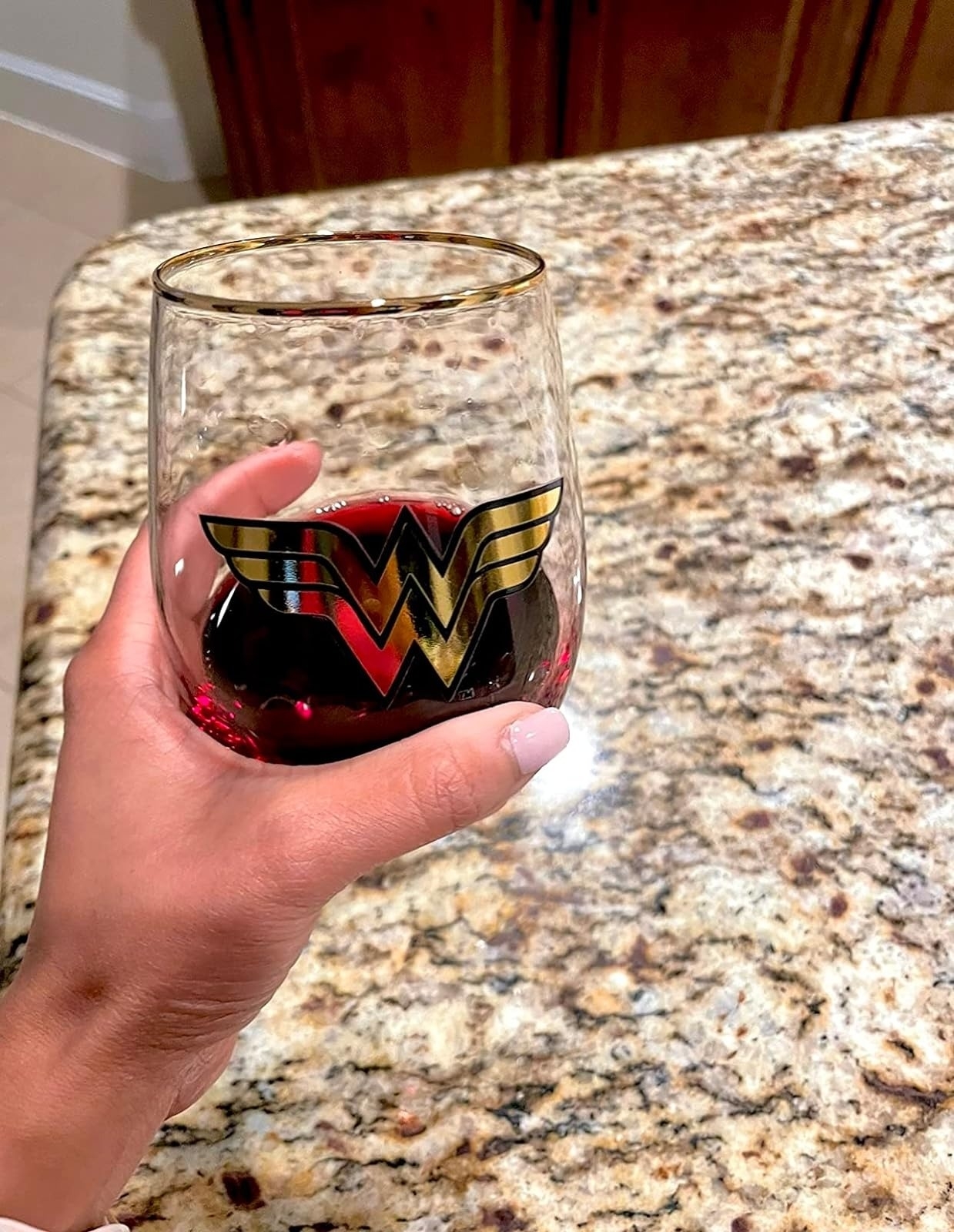 reviewer holding wine glass with Wonder Woman logo on the front