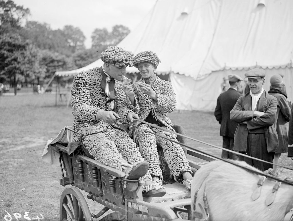 Two people sitting in a horse-drawn carriage wearing suits and caps completely covered with peanuts