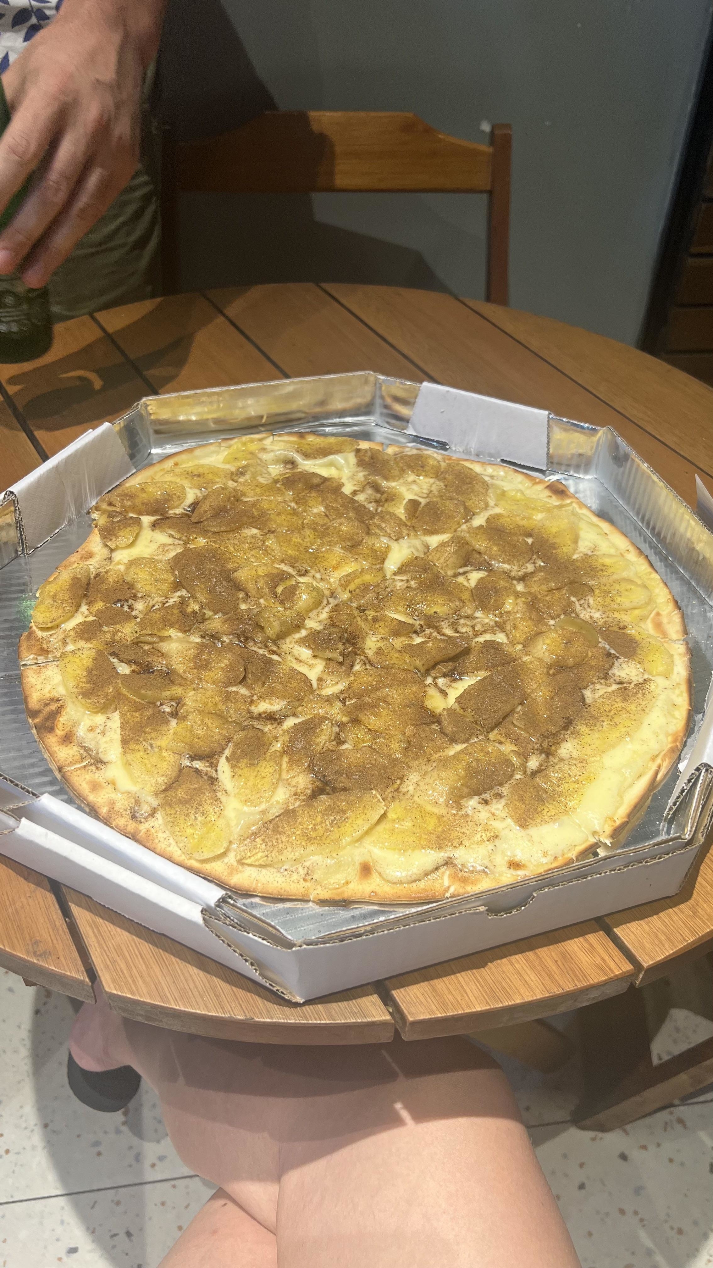 A pizza pie with banana slices and LOTS of cinnamon on a table