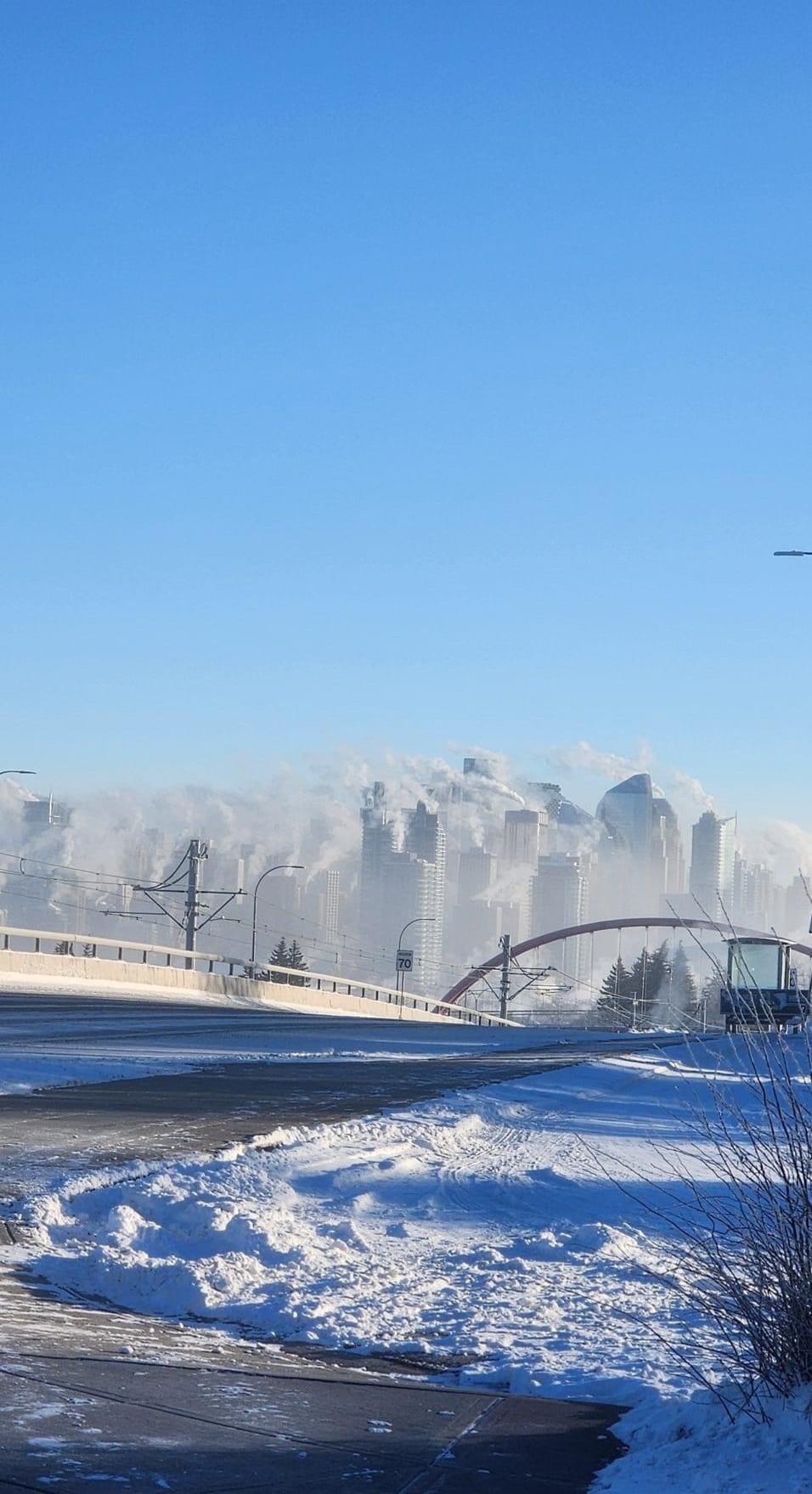 Mist/fog/smoke rising above skyscrapers in the background, with a snowy highway in the foreground