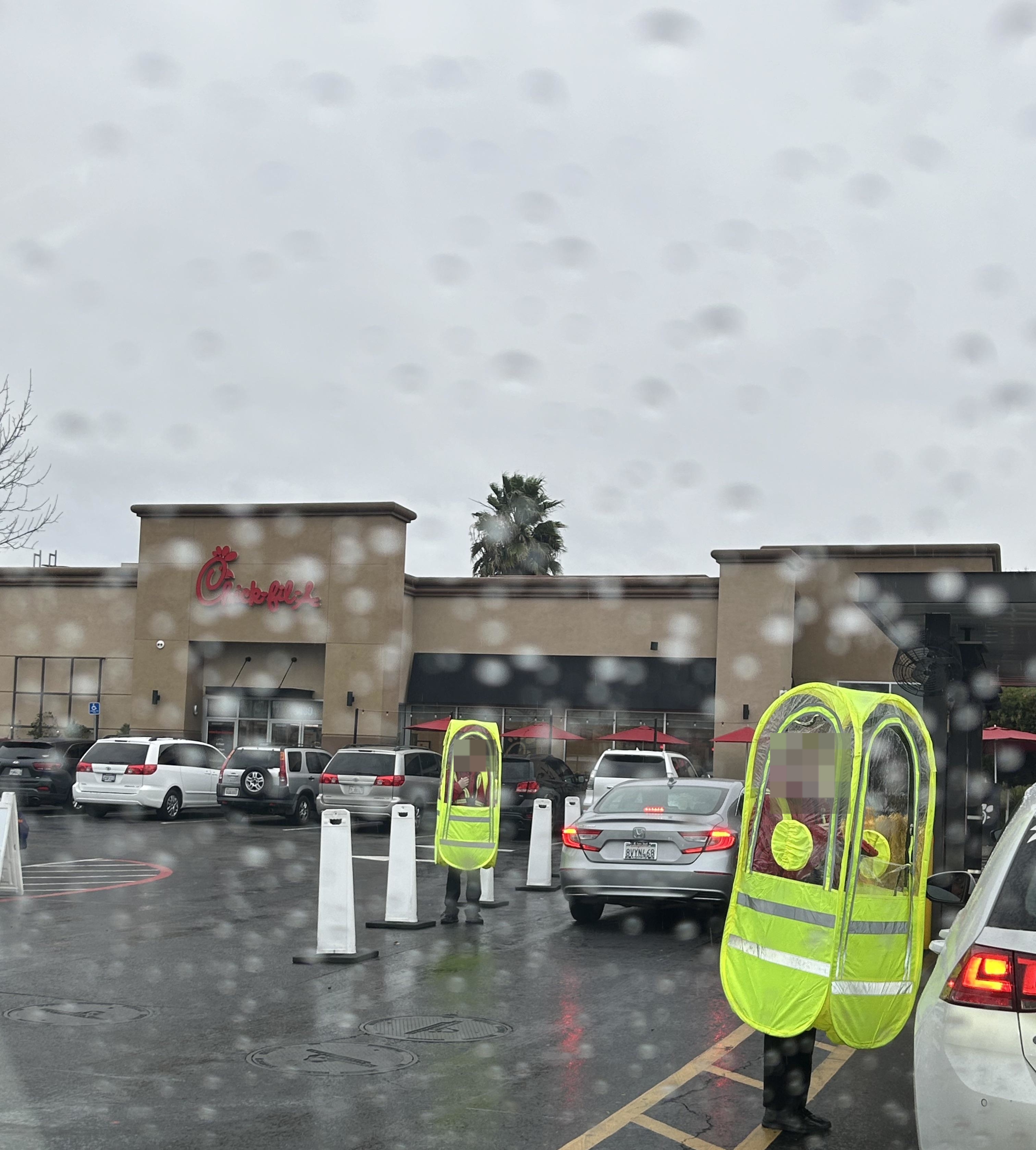 The Chick-fil-A parking lot in the rain, showing several people in neon-yellow, tubular bubbles with &quot;windows&quot;