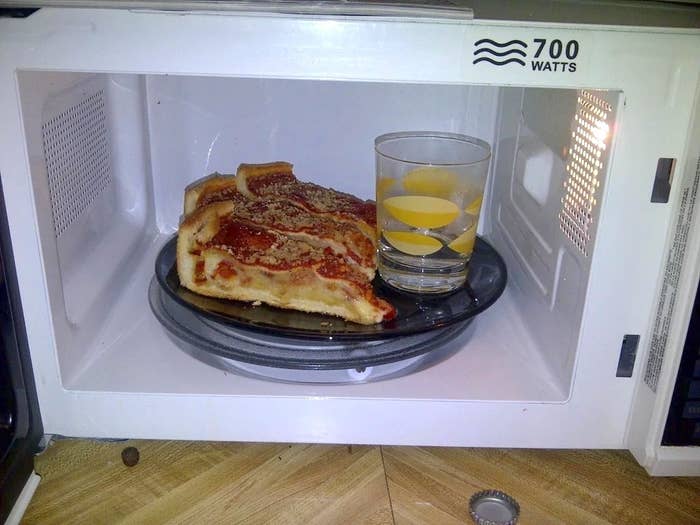 a glass of water in a microwave next to slices of pizza