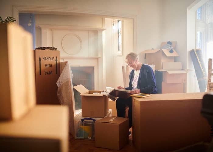 An old woman sorting through her belongs while packing boxes surround her