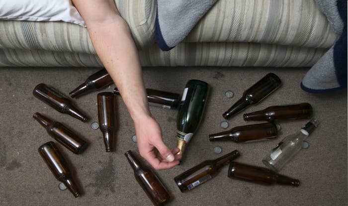 A bunch of beer bottles on the floor next to someone sleeping on a couch