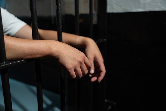 a person in jail with their arms leaning outside the bars