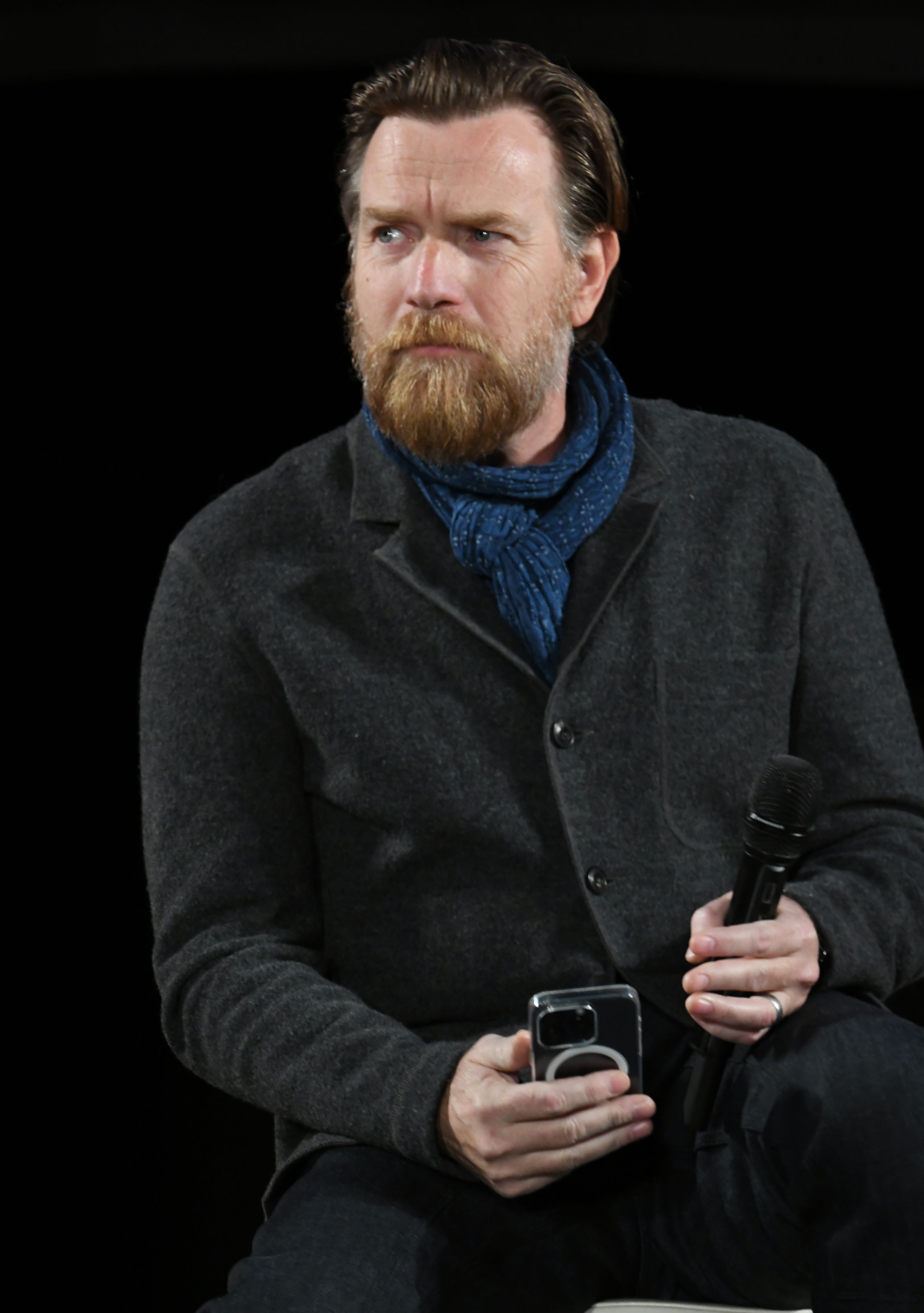 Close-up of Ewan wearing a cardigan and sitting and holding a microphone