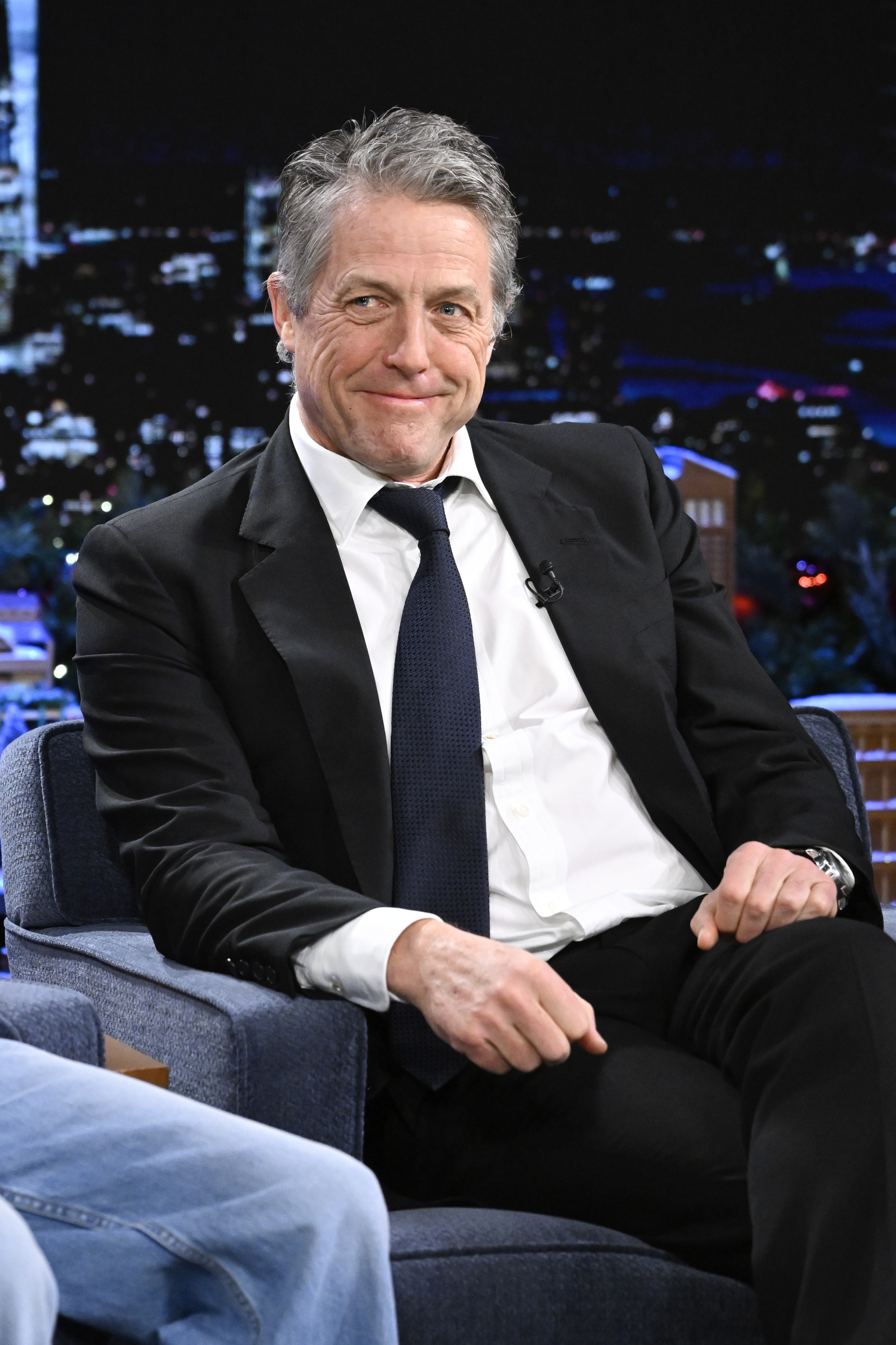Close-up of Hugh smiling in a suit and tie on a talk show