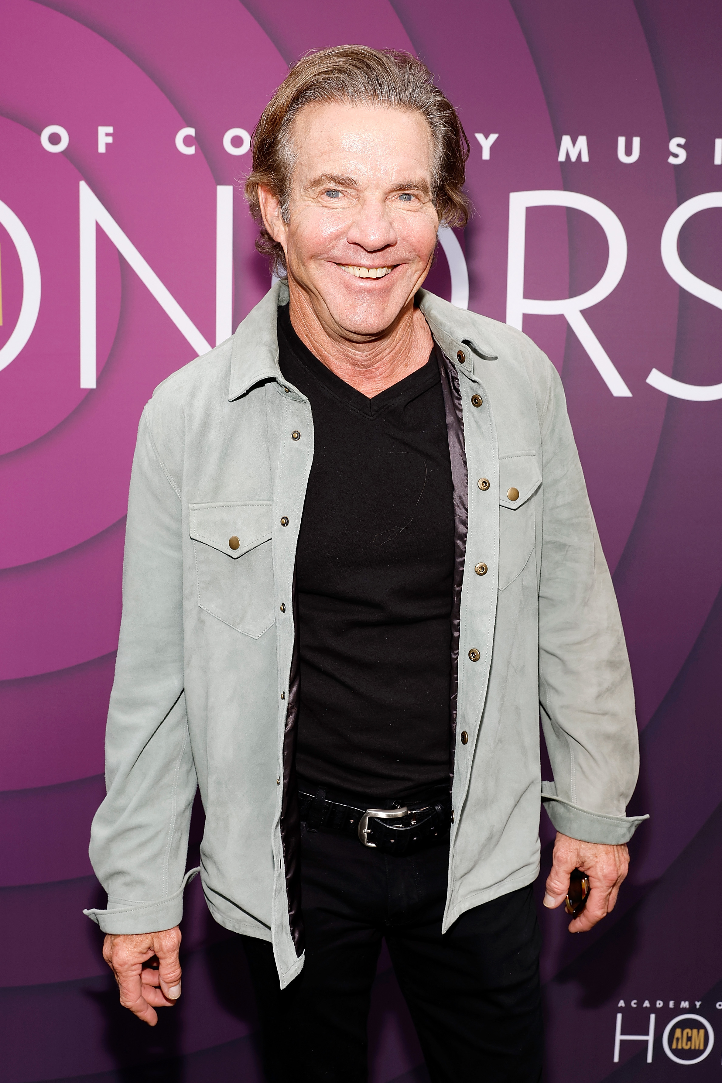 Close-up of Dennis smiling in a denim jacket at a media event