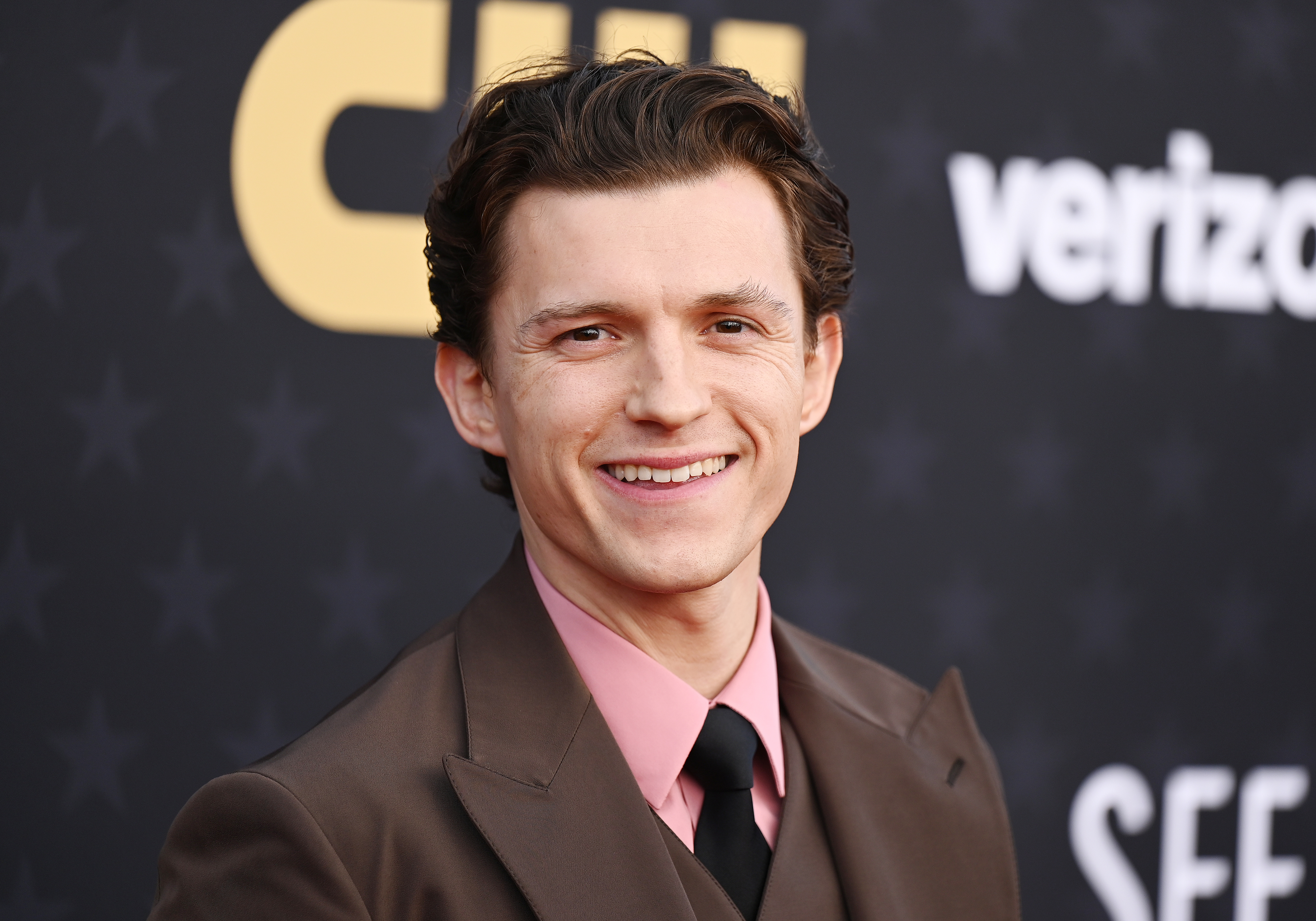 Close-up of Tom Holland smiling in a suit and tie at a media event