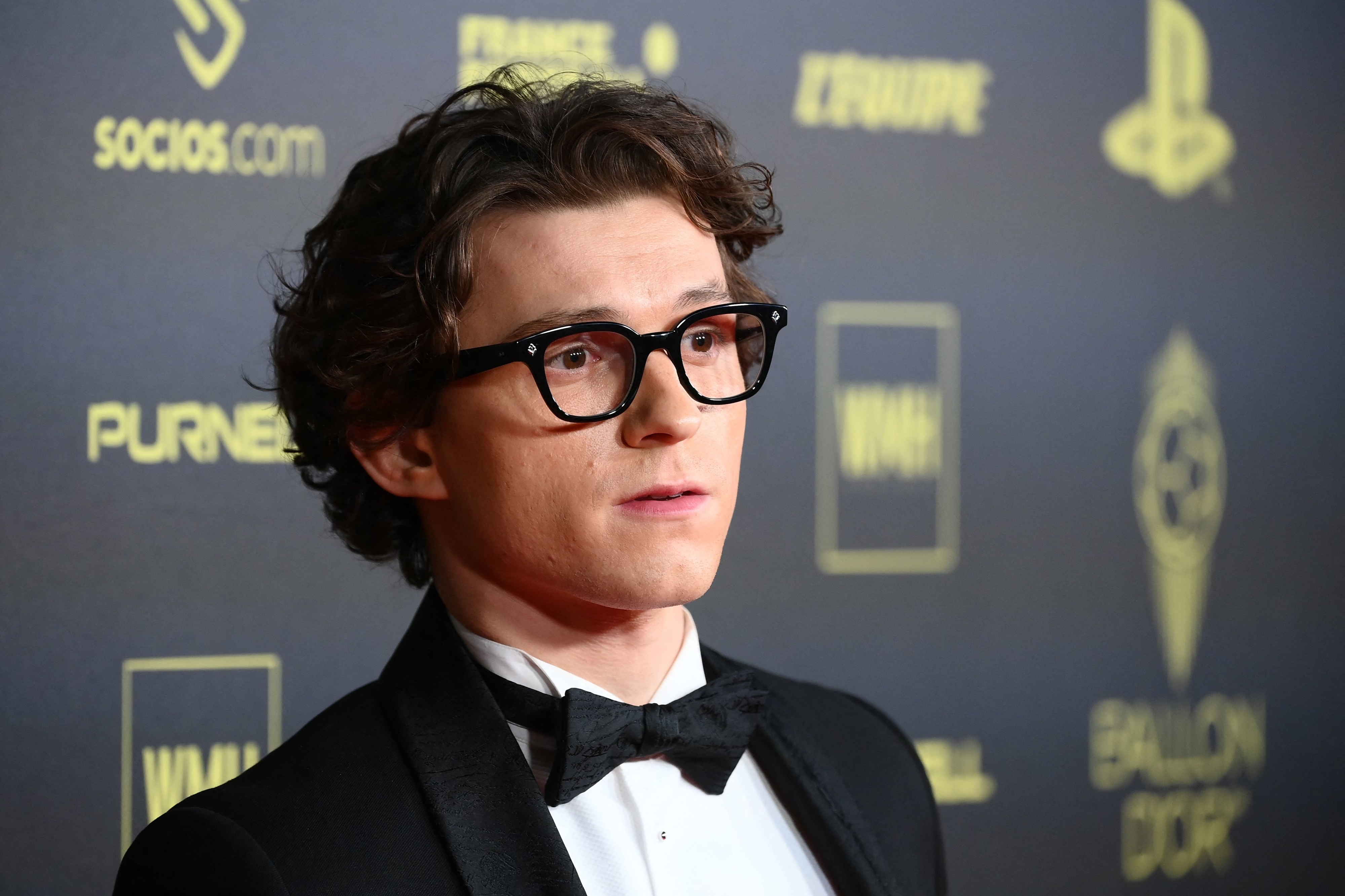 Close-up of Tom Holland in glasses and a suit and bow tie at a media event