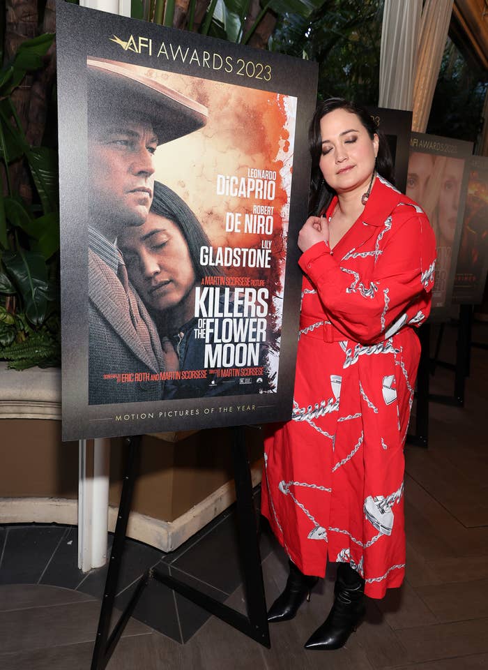 Lily Gladstone standing next to a poster for the film