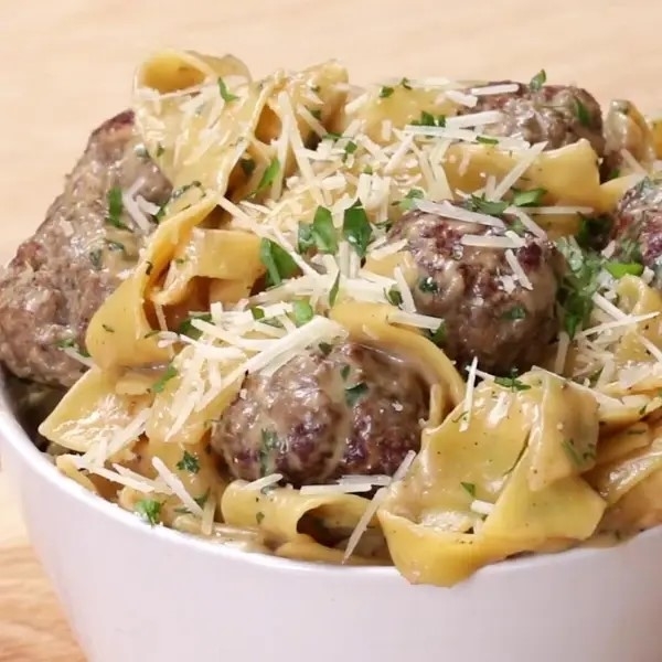 Pasta dish with meatballs, topped with grated cheese and parsley, served in a white bowl