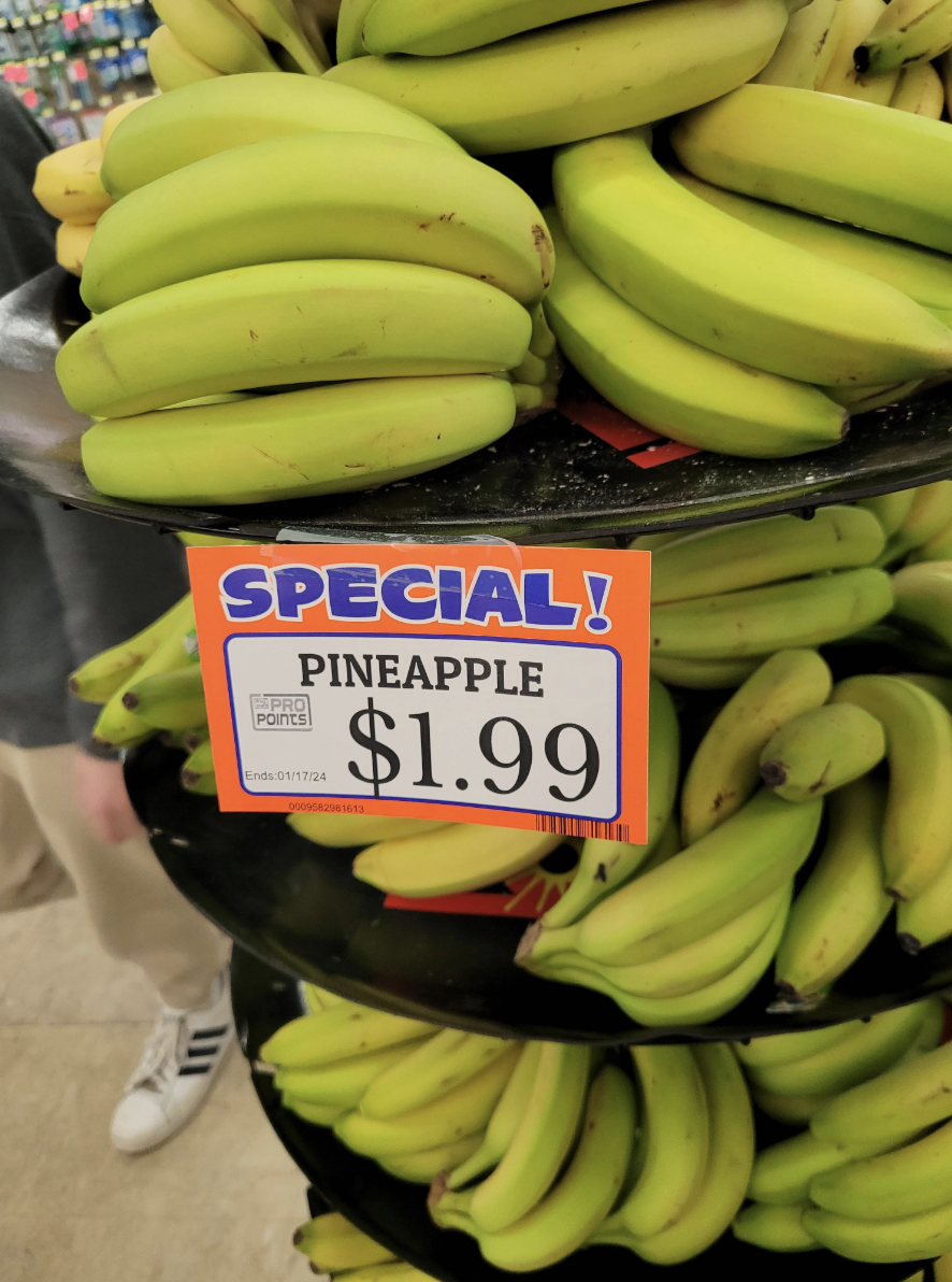 Bunches of bananas at the store with a &quot;Pineapple $2&quot; sign
