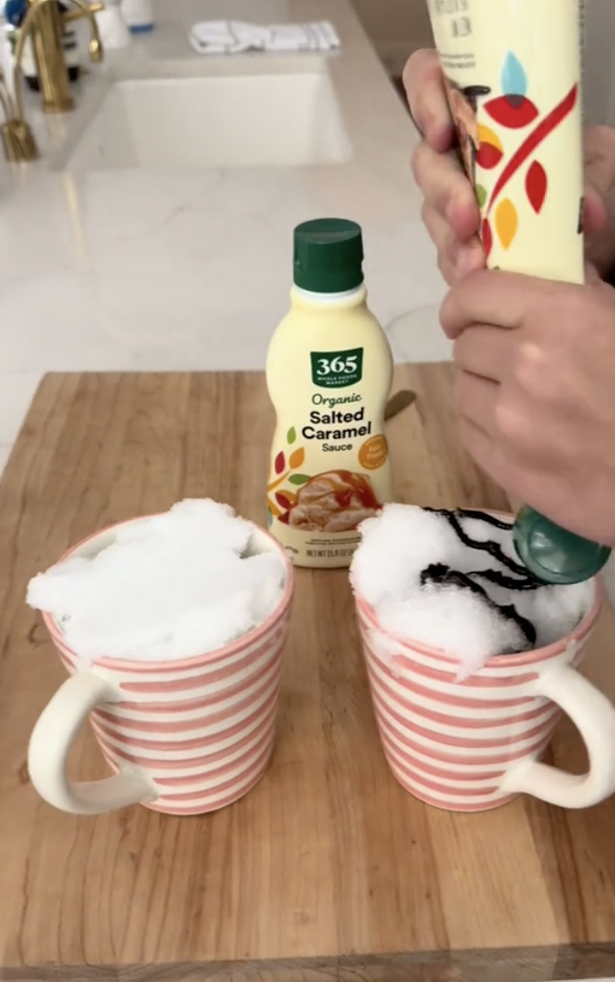 a screenshot from reese witherspoon&#x27;s tiktok of someone pouring chocolate syrup onto a mug of snow