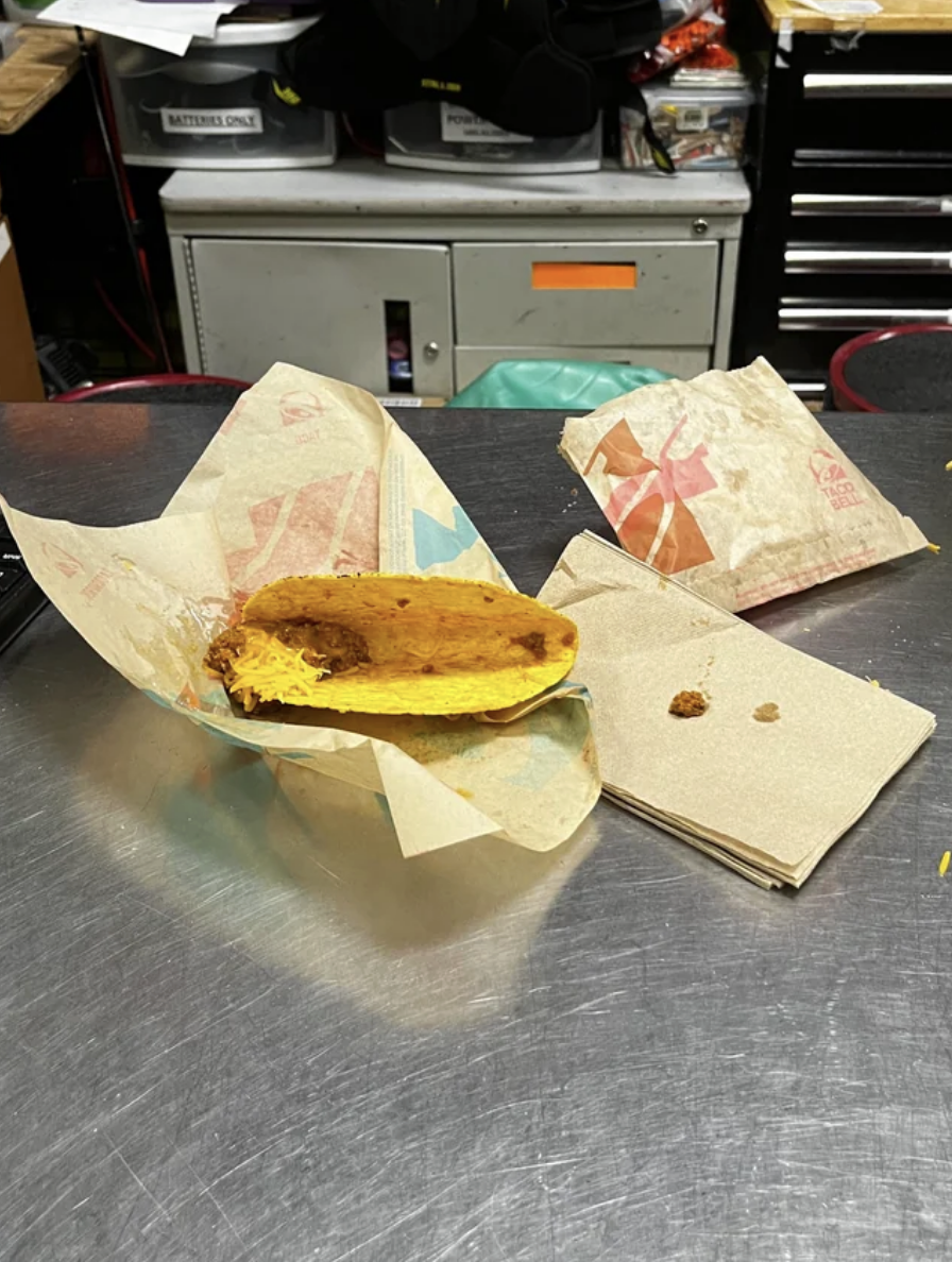 A hard taco in wrapping with a minute amount of shredded cheese and beans at one end