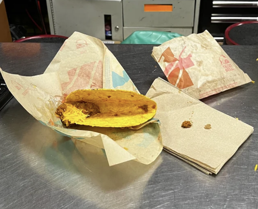 A hard taco in wrapping with a minute amount of shredded cheese and beans at one end