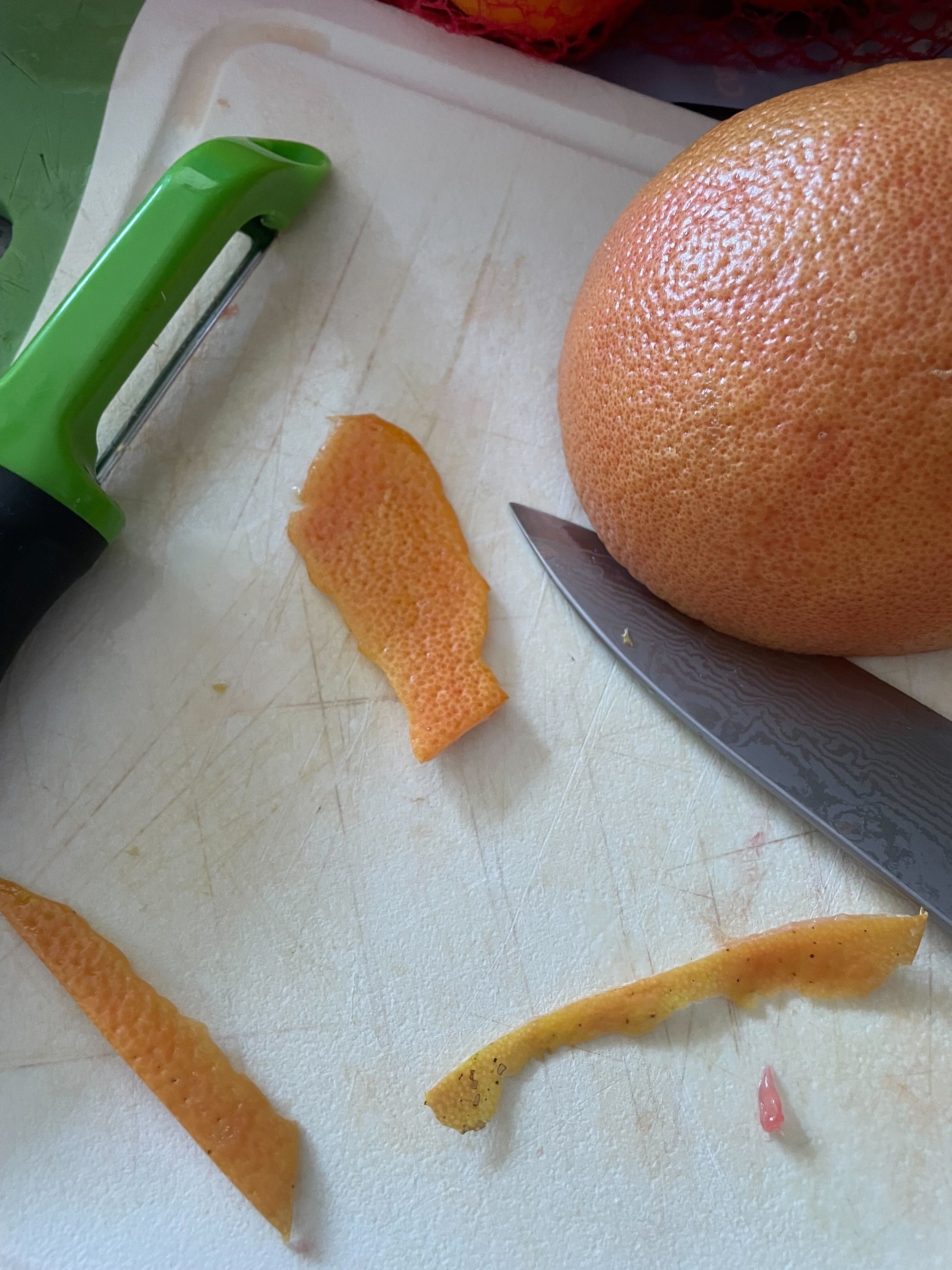cutting board with grapefruit peels, knife, and vegetable peeler
