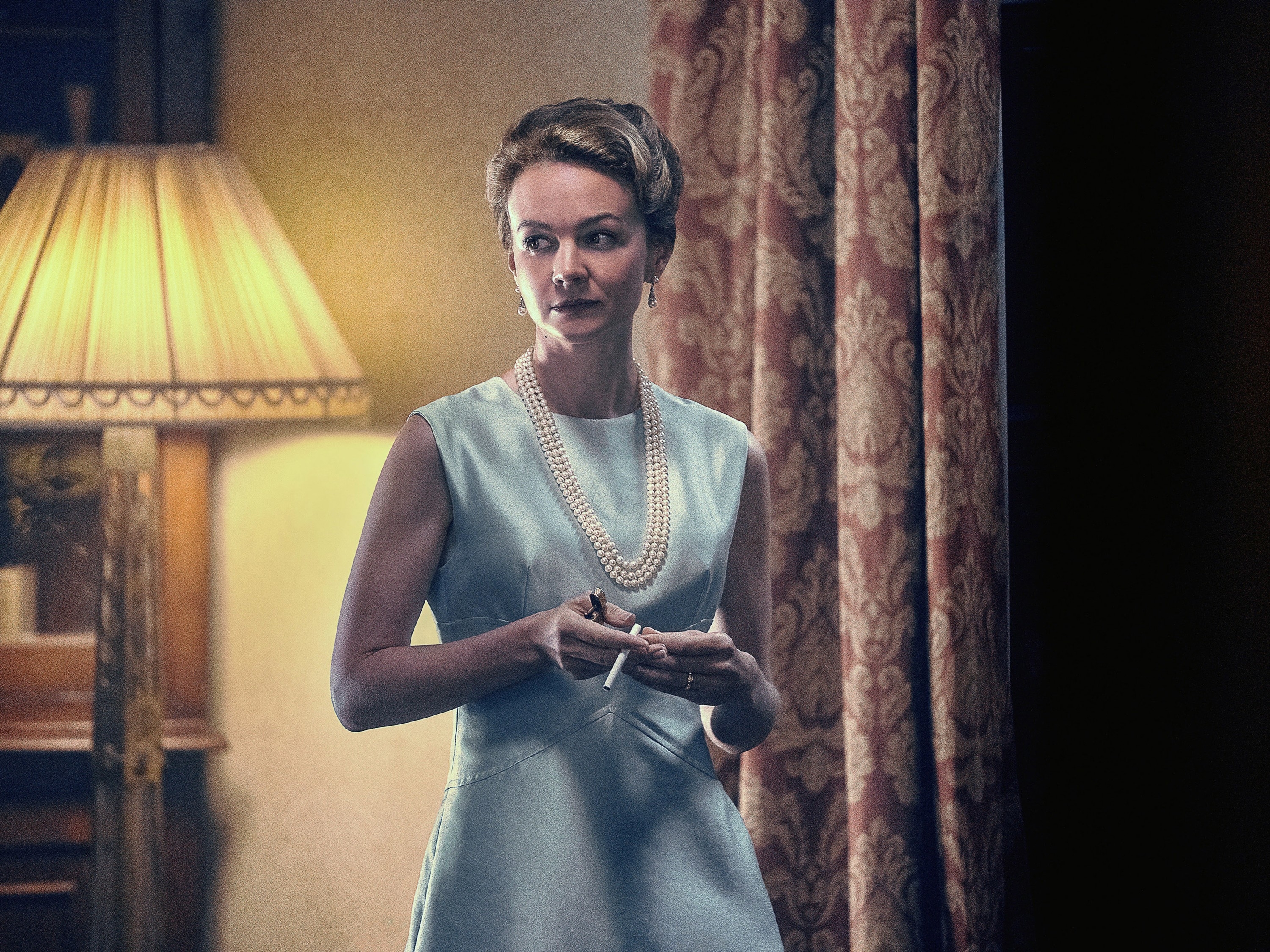 Close-up of Carey in a sleeveless dress and pearls, holding a cigarette