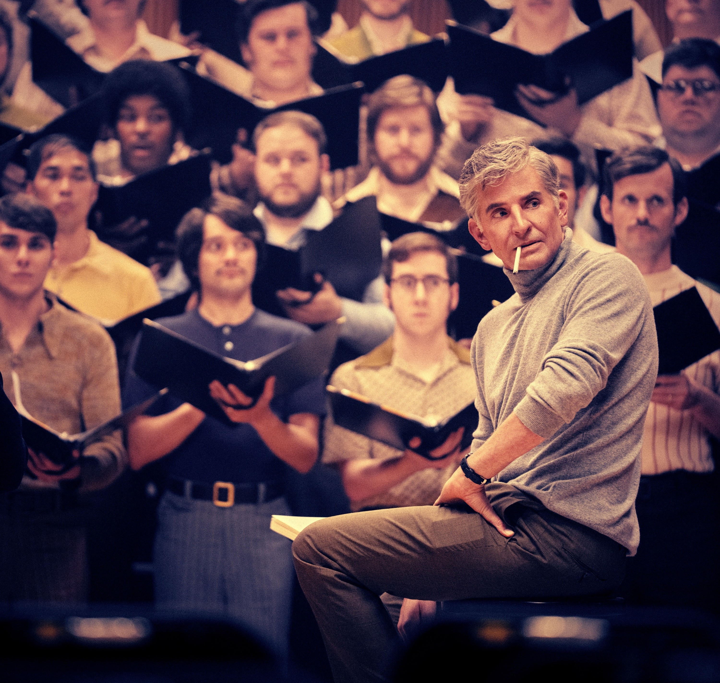 Close-up of Bradley sitting in front of a chorus and smoking a cigarette