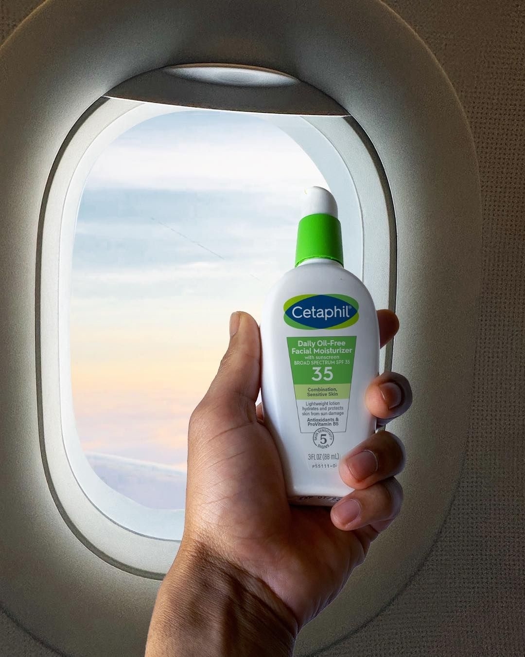 A model holding the sunscreen in front of an airplane window