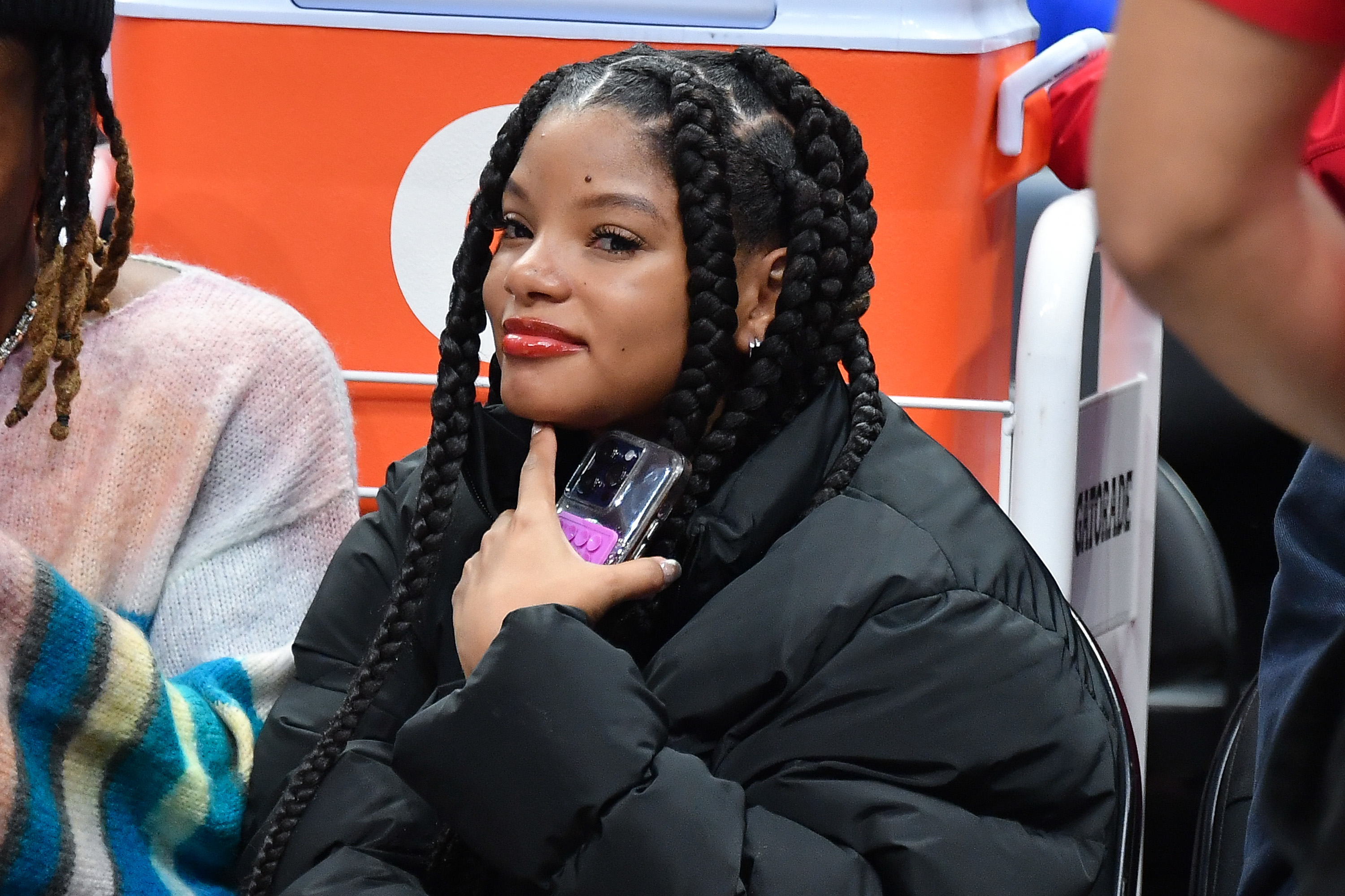 A close-up of Halle sitting, wearing a puffy jacket, and holding a cellphone