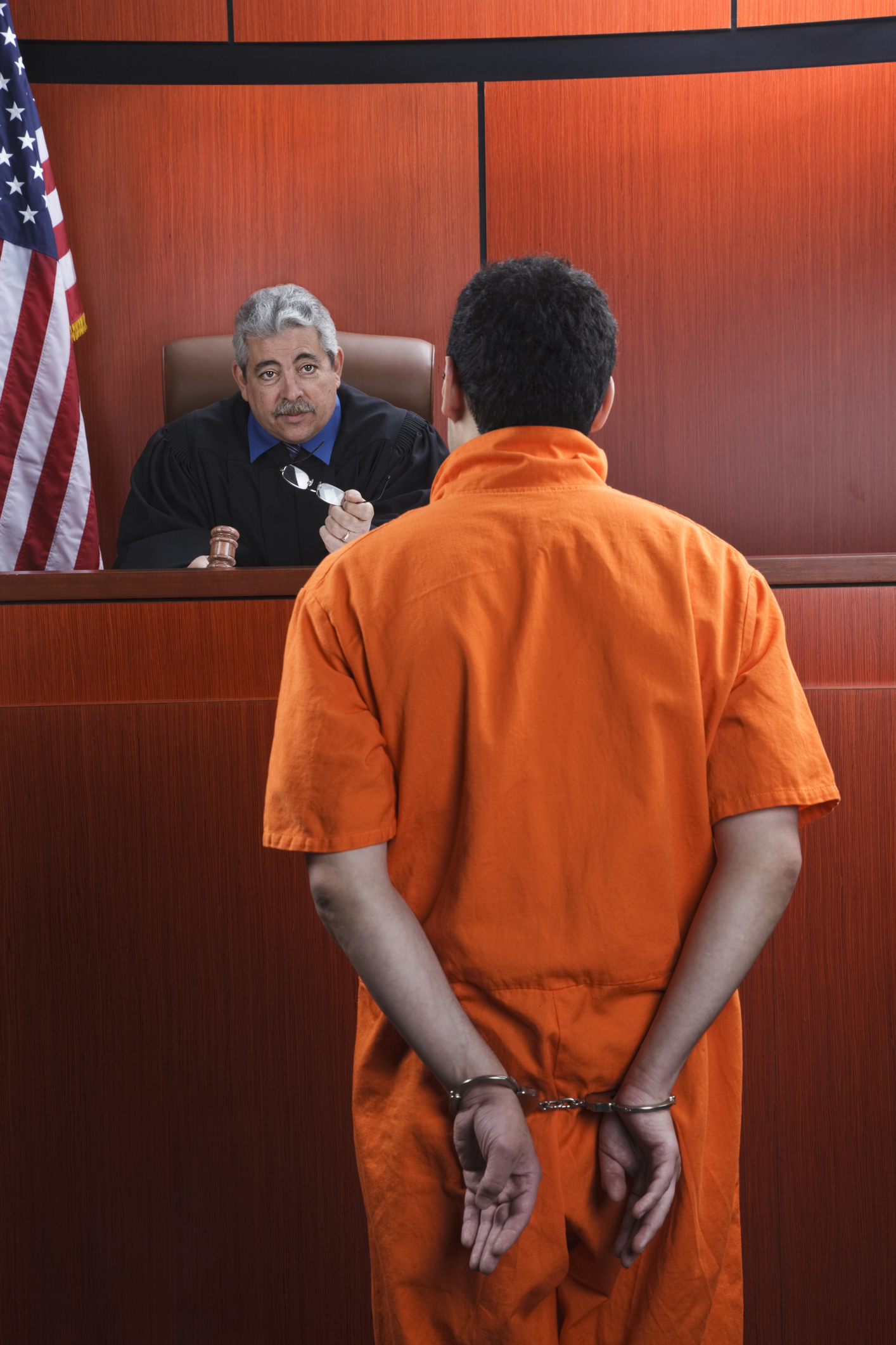 A handcuffed man in orange standing in a courtroom in front of a judge