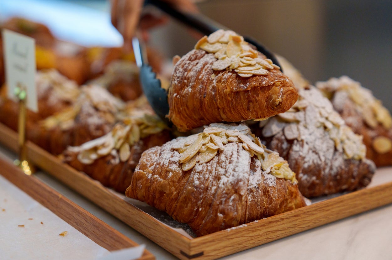 Someone grabbing an almond croissant from a display with tongs