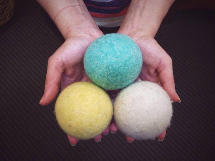 A person holds three colorful wool dryer balls in their hands