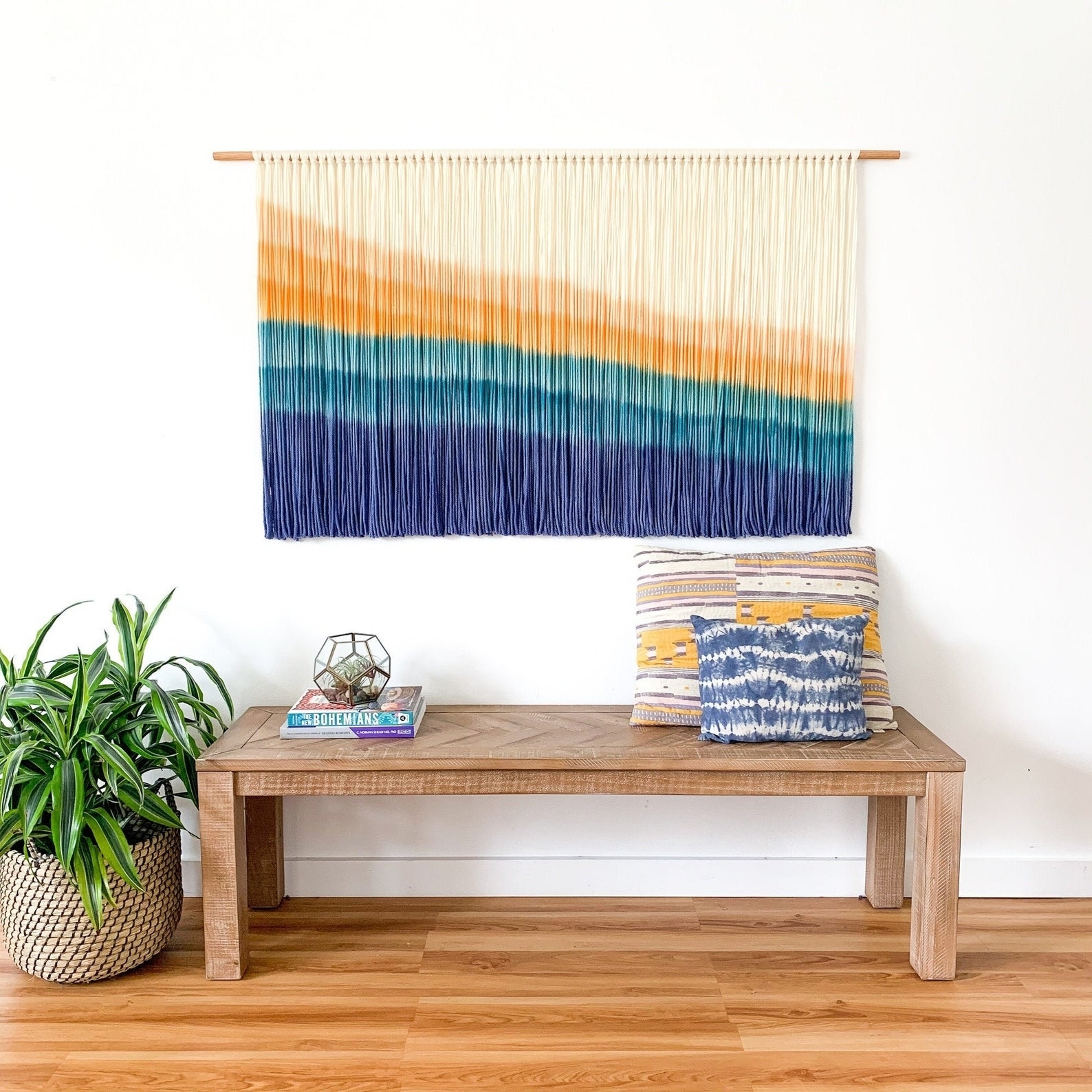 the large yellow, orange, and blue, macrame hanging above a bench