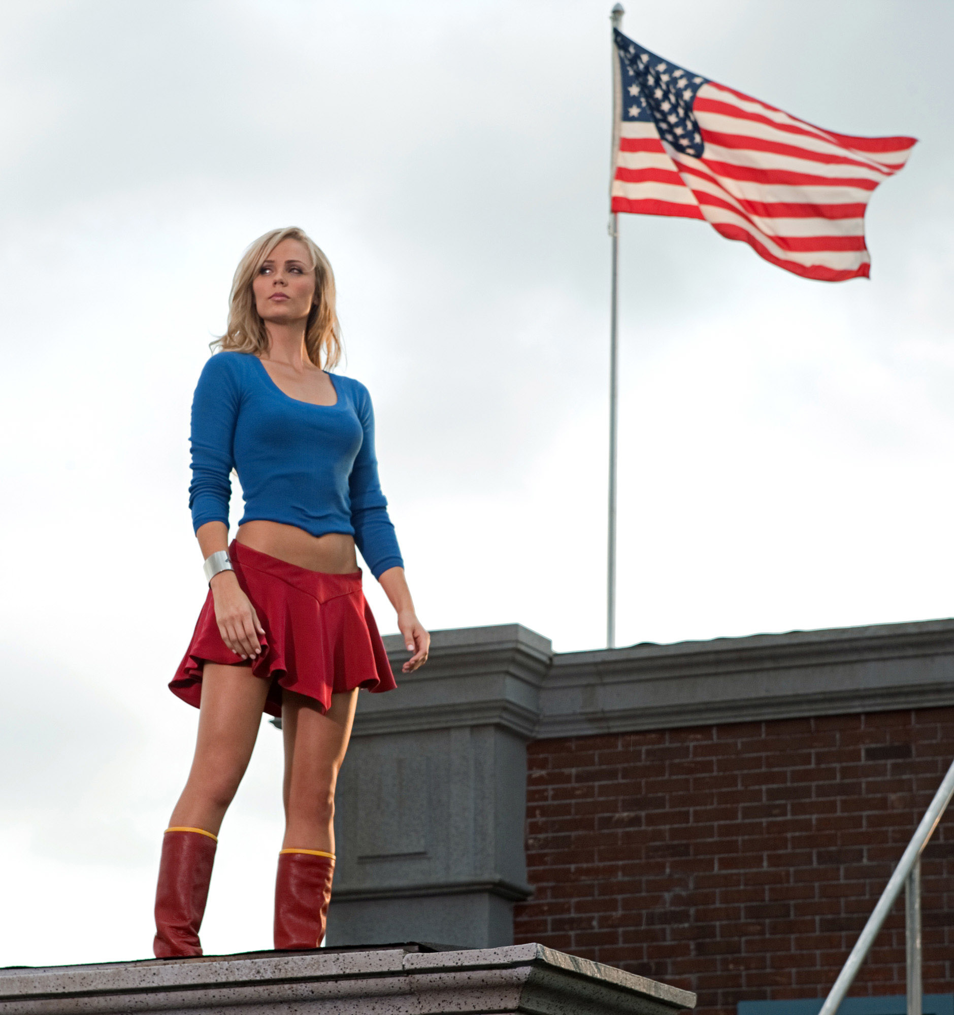 Laura Vandervoort standing on a roof with the American flag flying behind her in a scene from &quot;Smallville&quot;