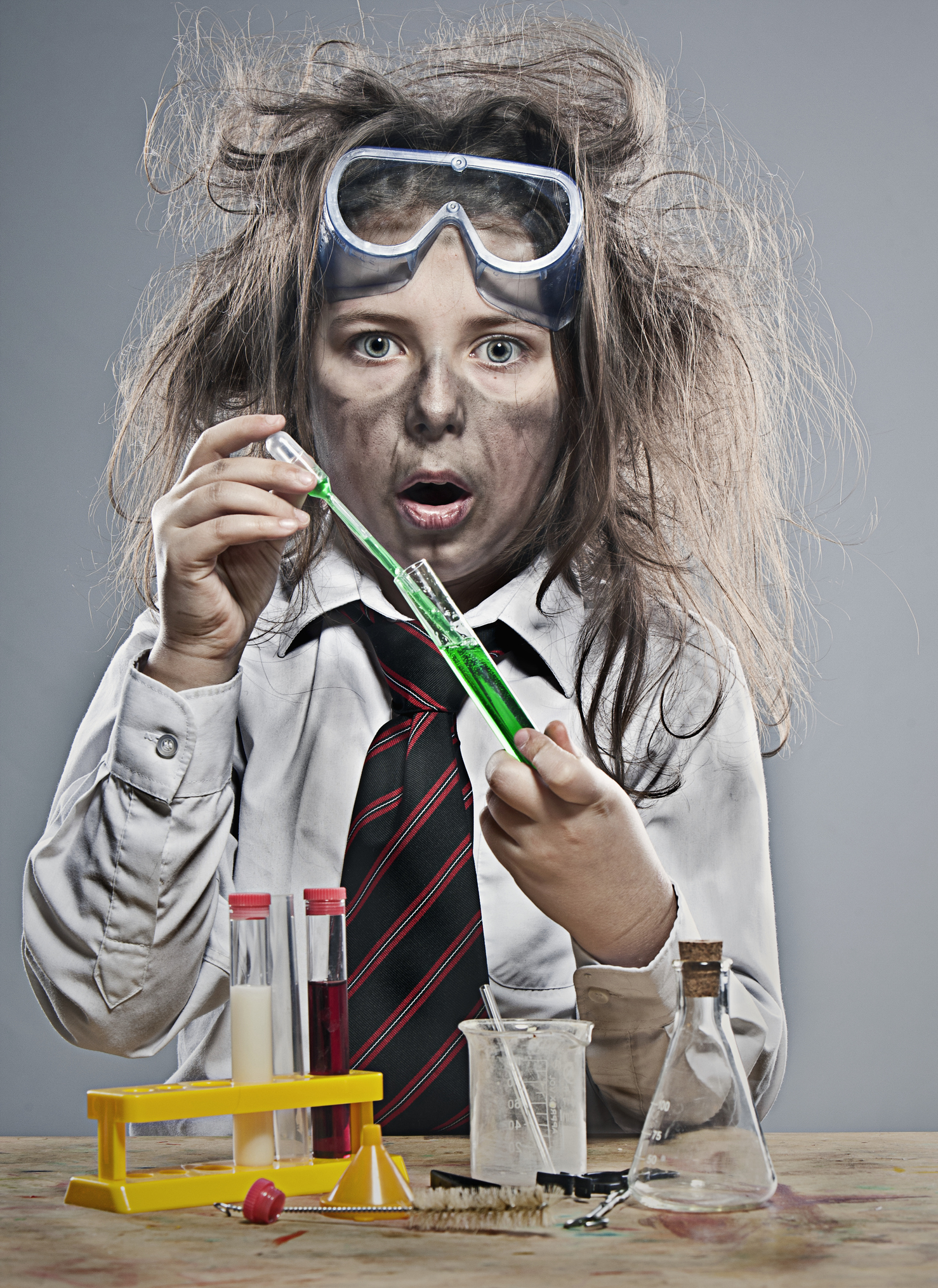 A woman with smudges on her face and goggles holding a test tube containing a liquid