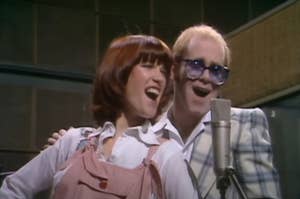 Elton John and Kiki Dee singing into a microphone together.