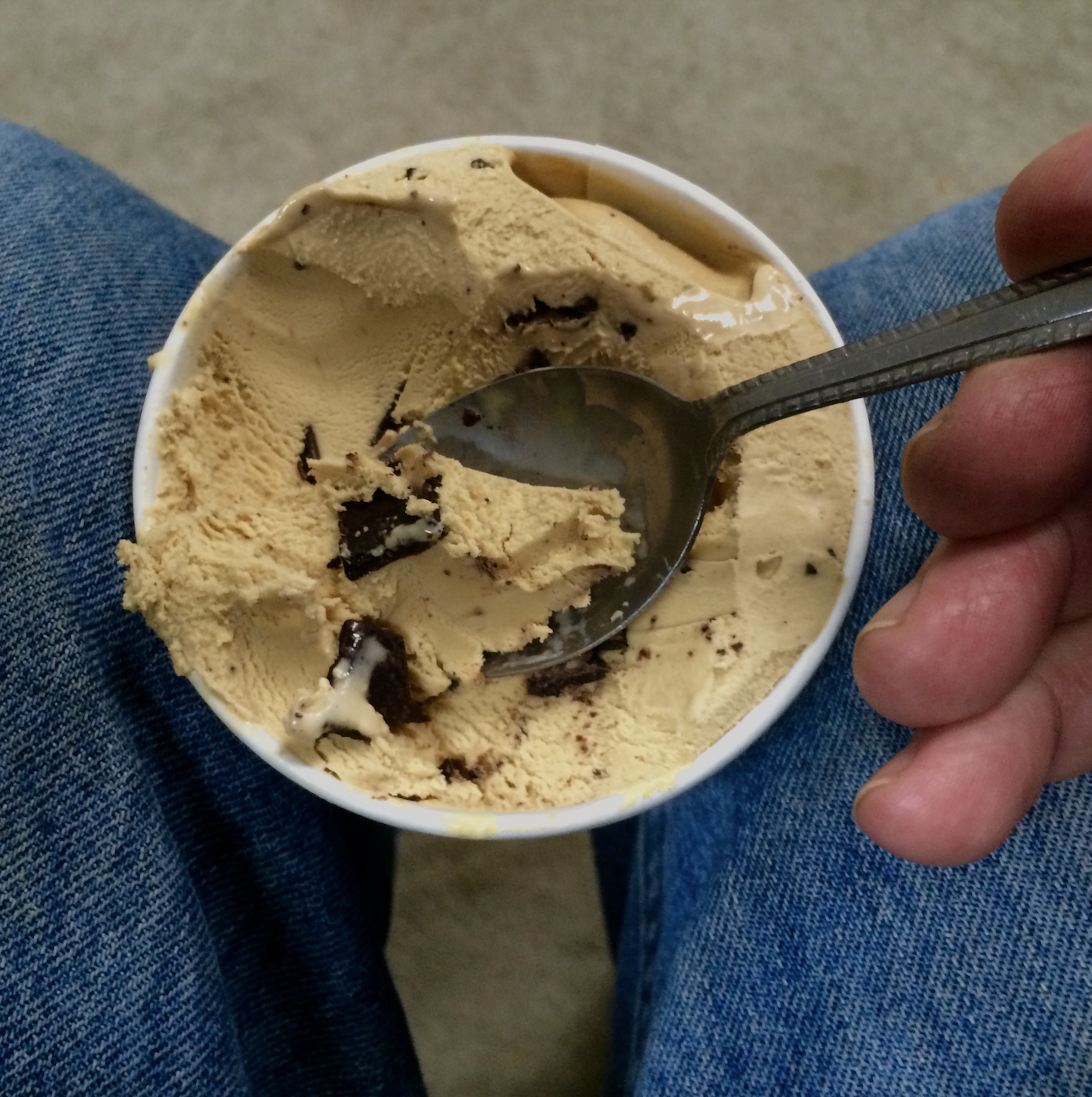 A spoon in a tub of ice cream in someone's lap