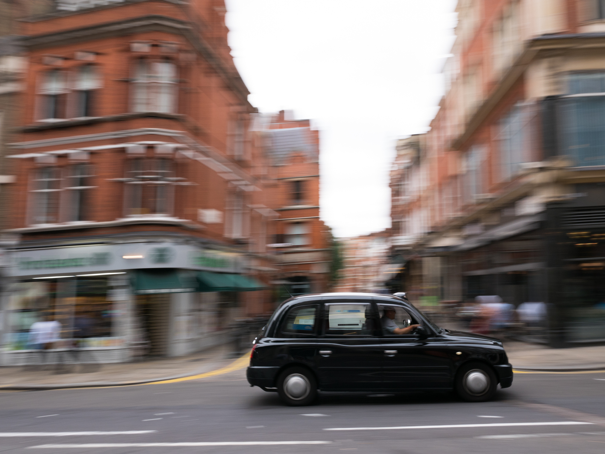 A black taxi cab flying through the streets of London.