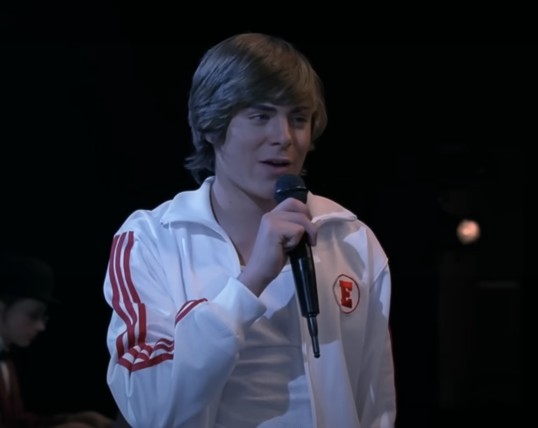 Close-up of Zac as Troy Bolton speaking into a microphone