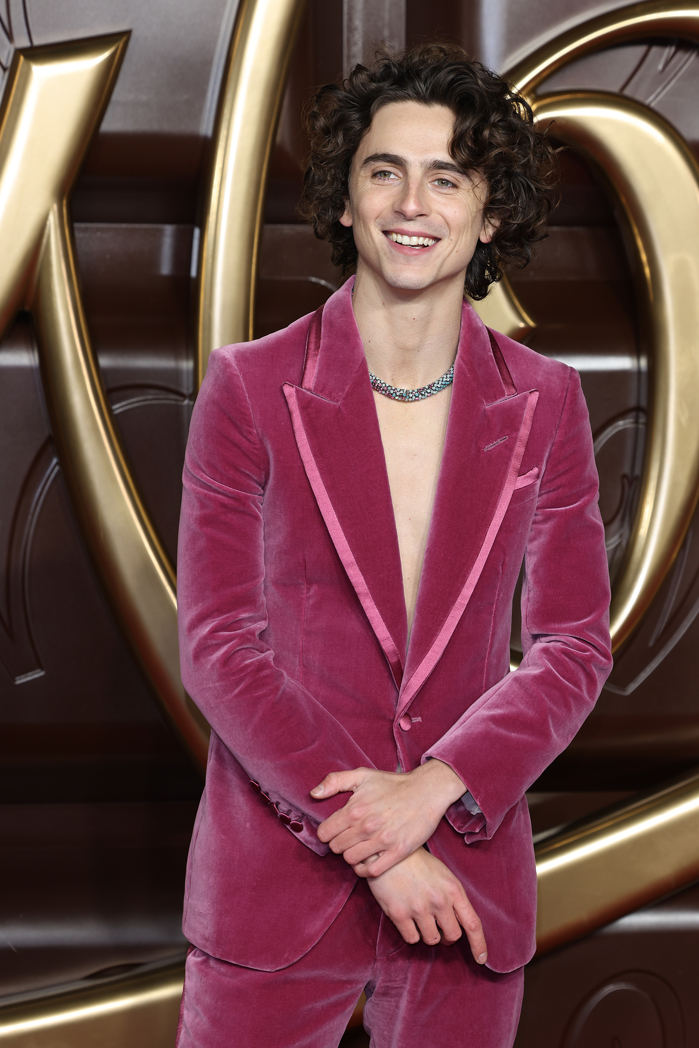 Close-up of Timothée smiling at a media event and wearing a pink velvet suit, no shirt