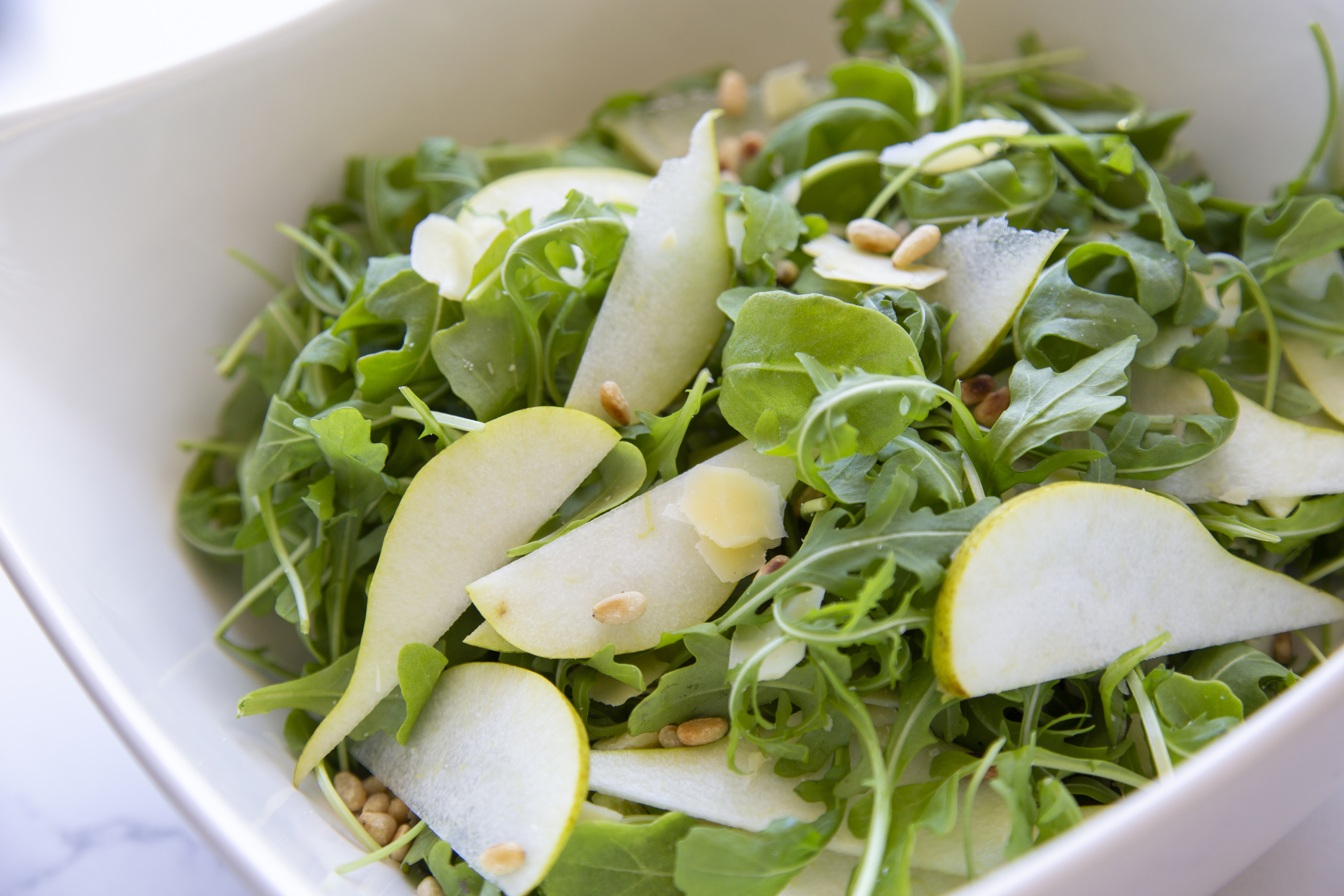 A bowl of rocket, pear, Parmesan and pine nuts.