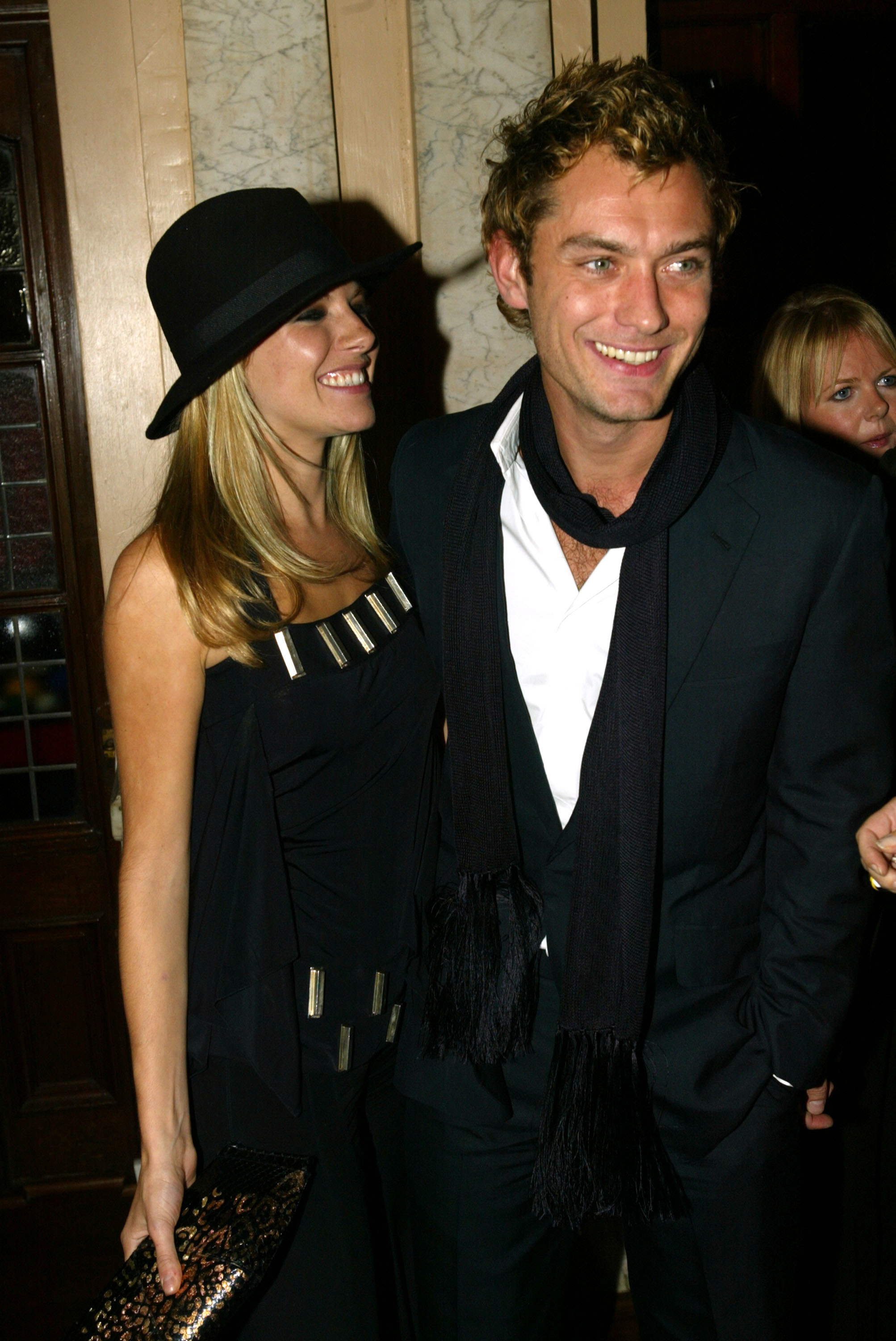 She's smiling and wearing a hat and sleeveless outfit; he's smiling and wearing a suit and shirt