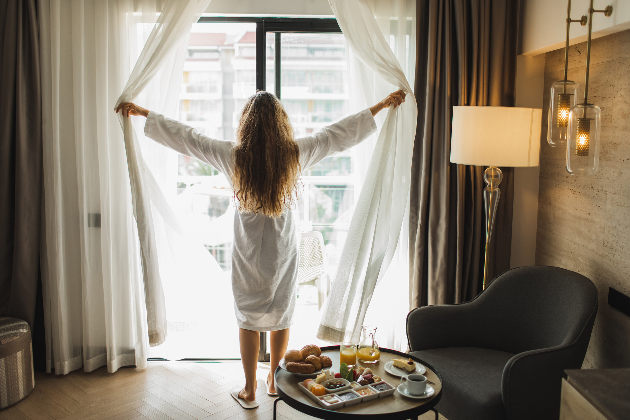 A woman opening curtains and letting the sunlight into her hotel room