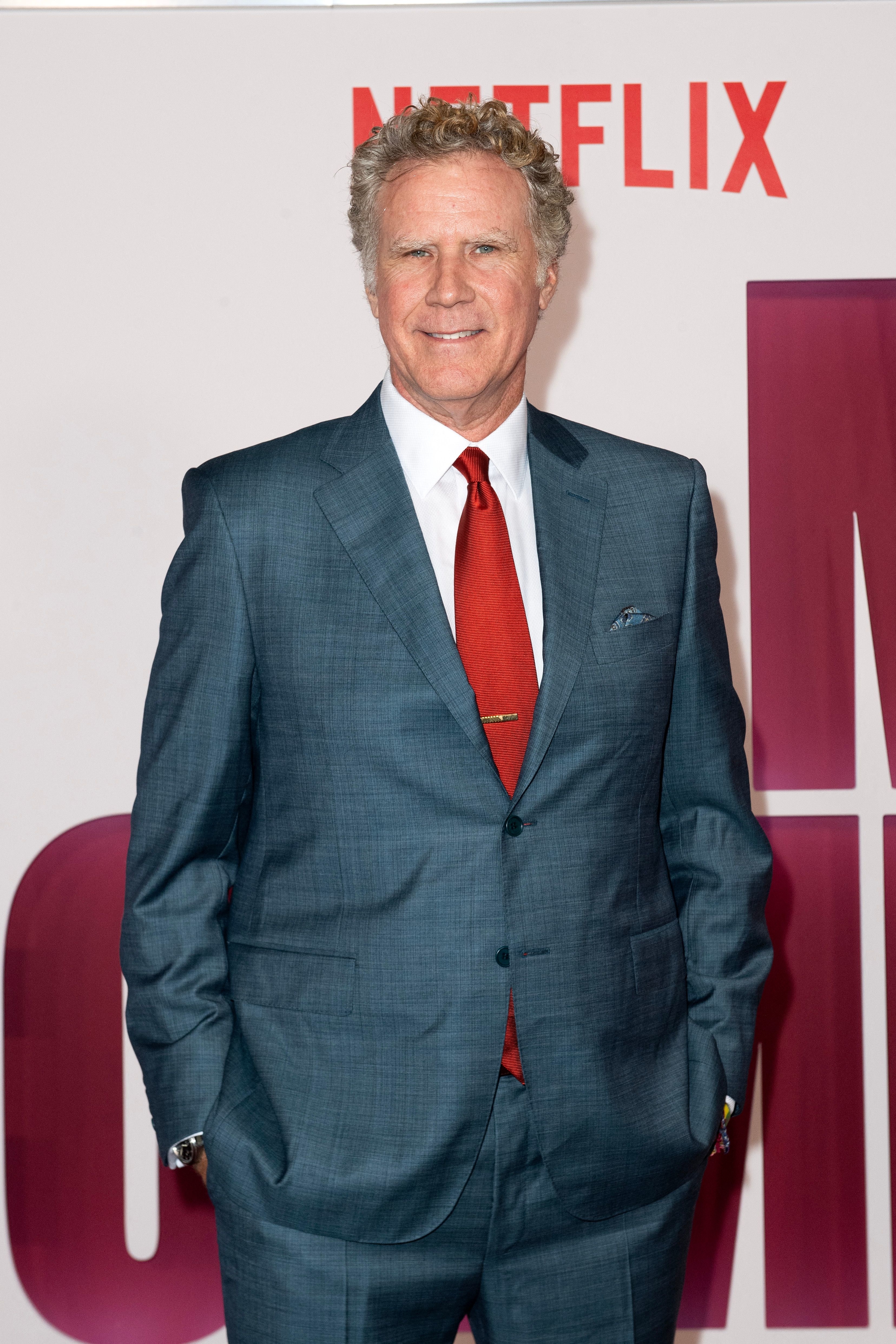 Will in gray suit and red tie standing against a backdrop with Netflix logo