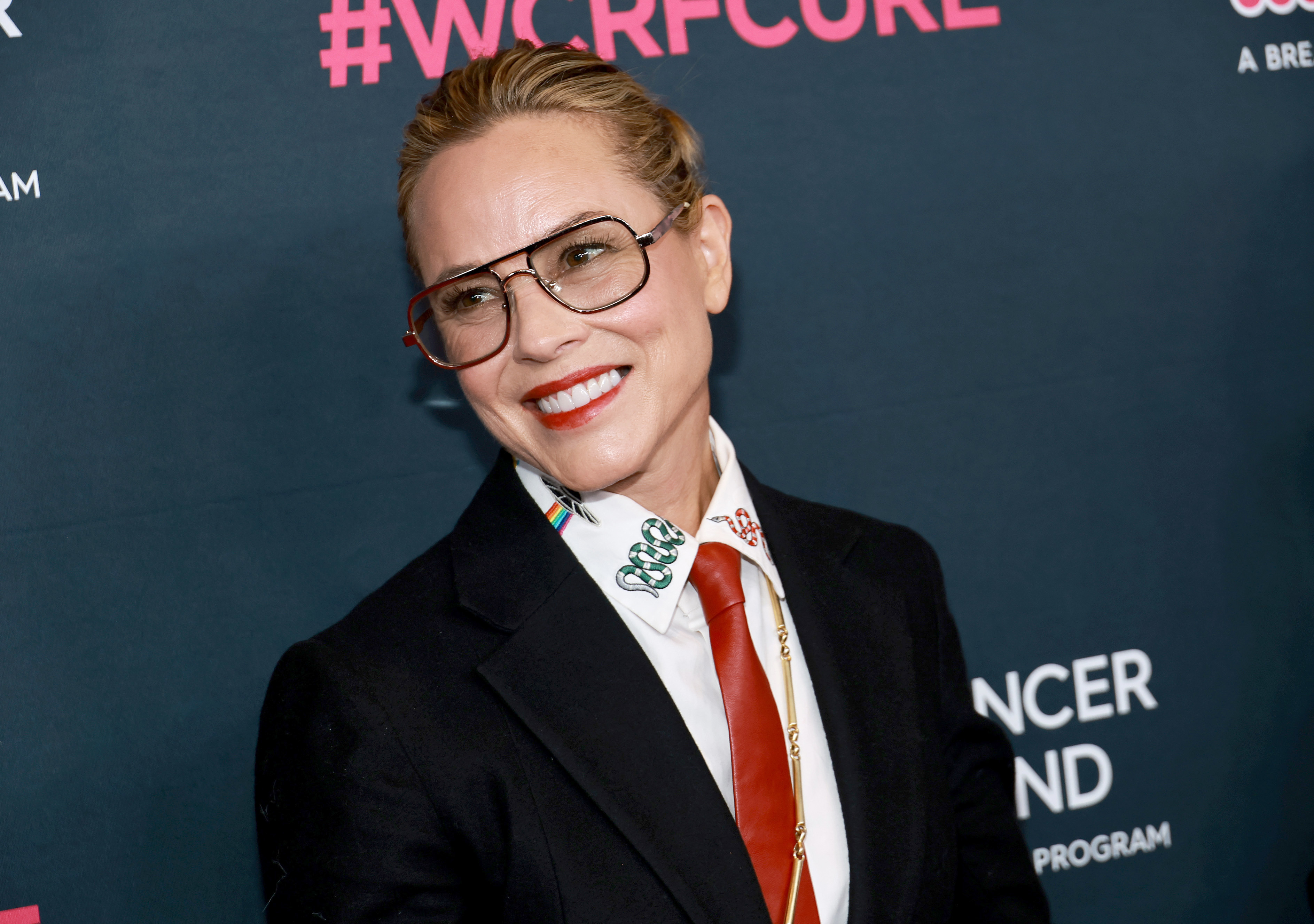 Maria smiling at a media event wearing a suit and tie