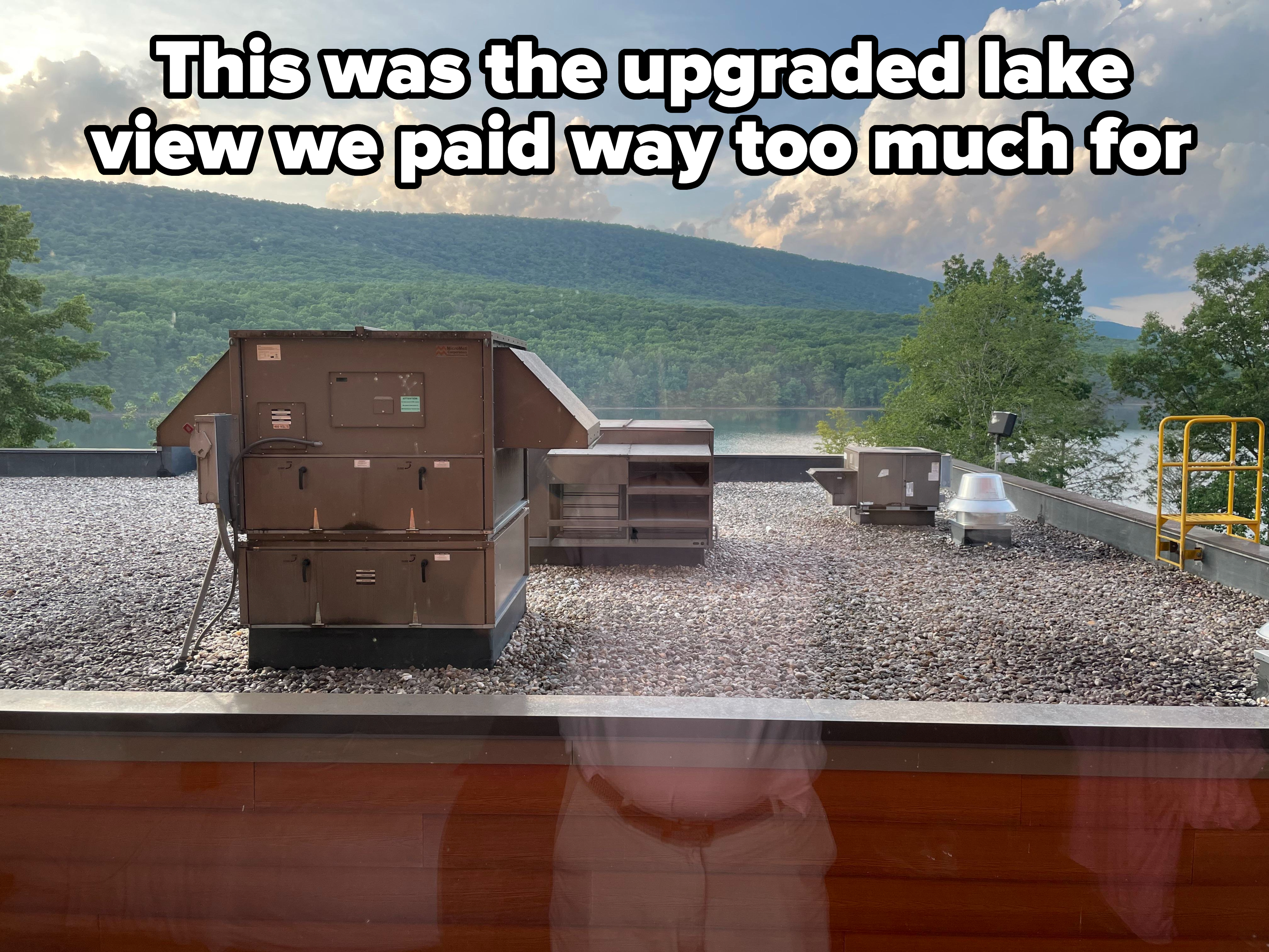 View from a window of a gravel roof with storage items on it and hills behind it