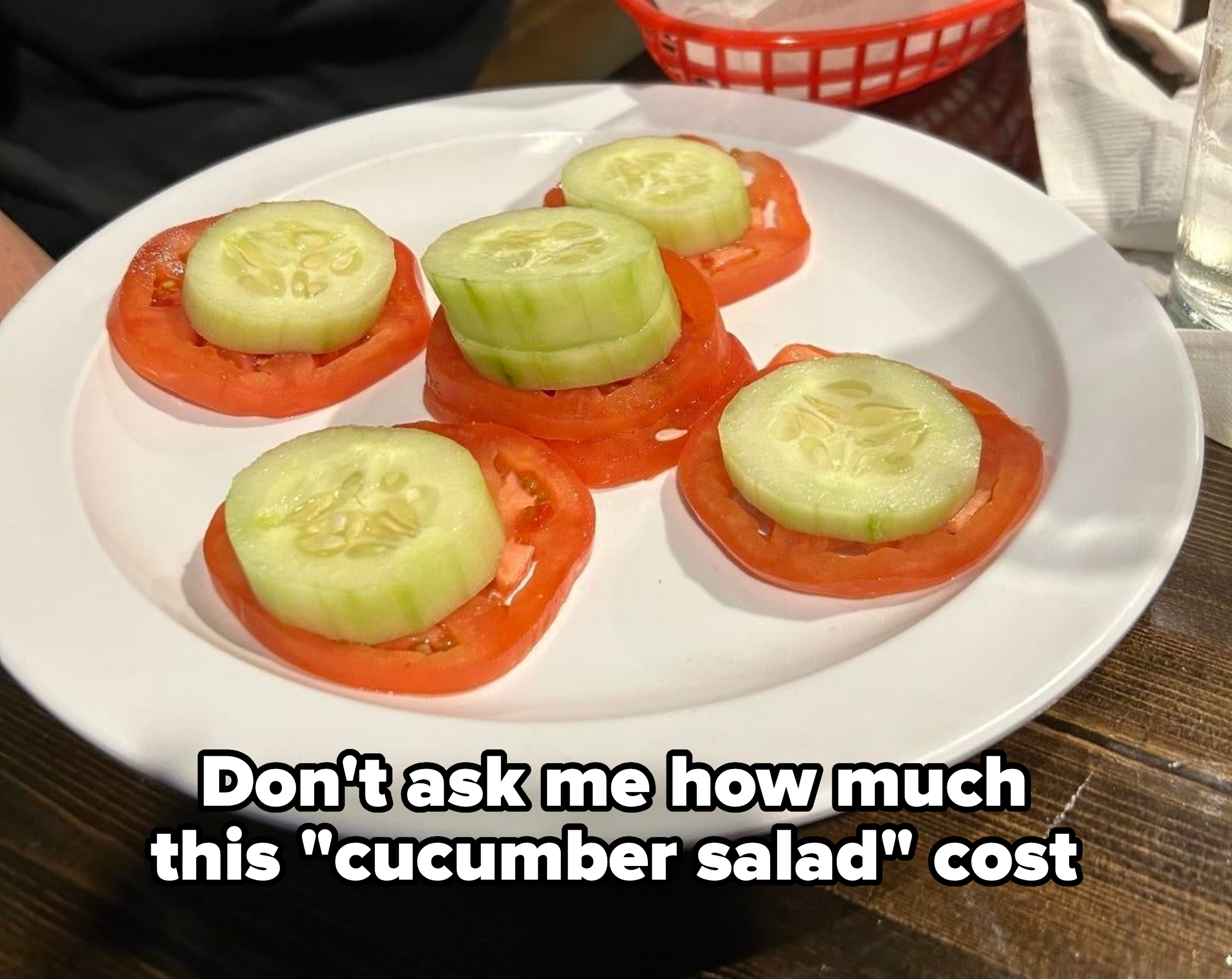 A plate with five tomato slices with pieces of cucumber on them, with caption, "Don't ask me how much this 'cucumber salad' cost"
