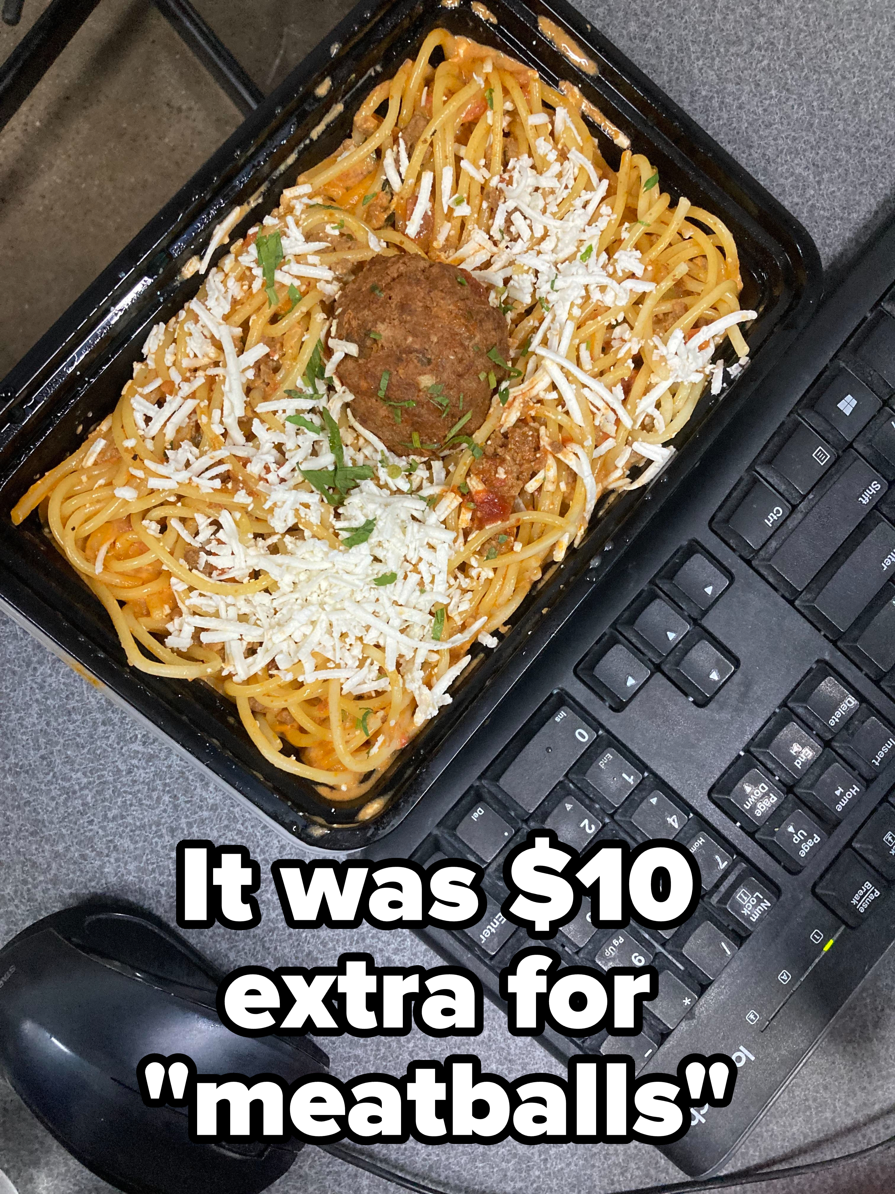 A takeout container of spaghetti with one meatball, with caption, "It was $10 extra for 'meatballs'"