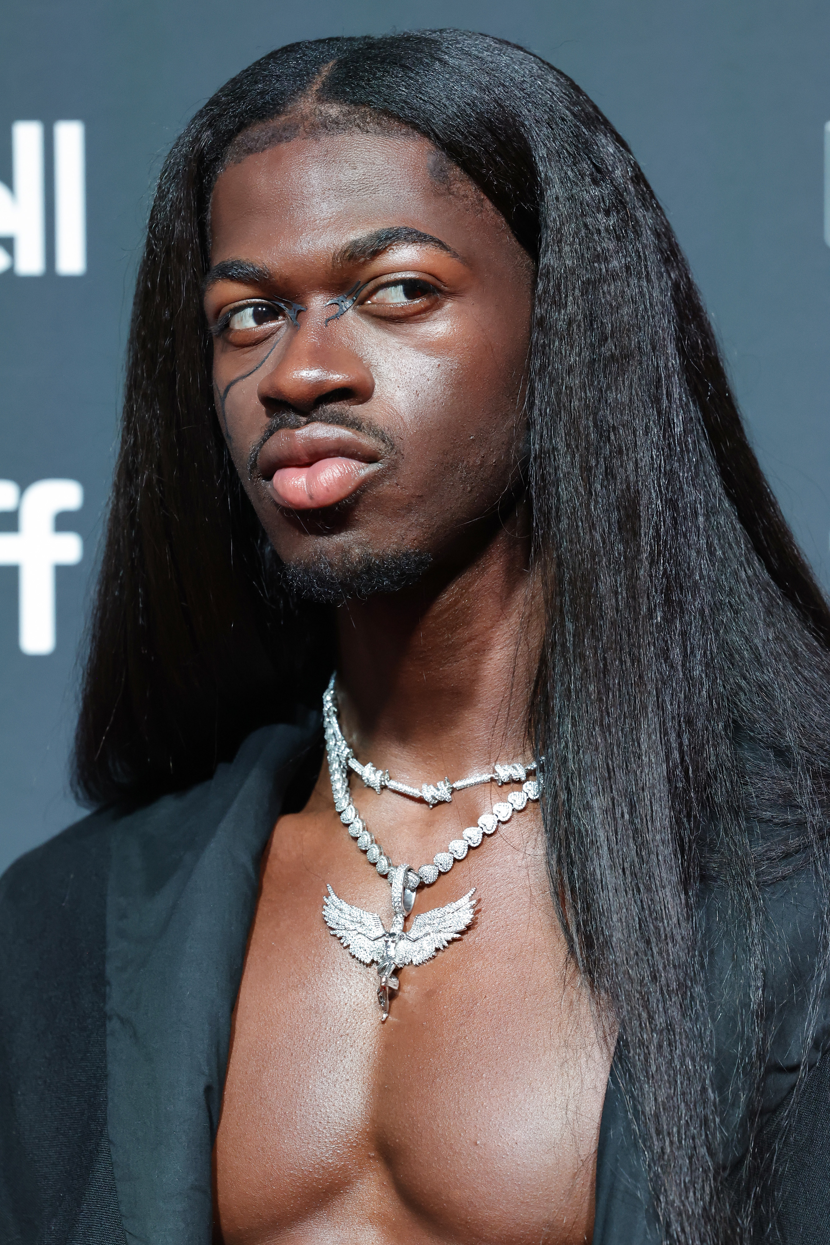 Close-up of Lil Nas X wearing a necklace and open jacket showing a bare chest