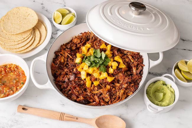 Le Creuset pot filled with pulled pork, accompanied by tortillas, limes, salsa, and guacamole for shopping article