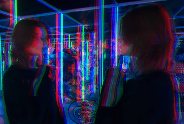 person looking at their reflection with color lights all around