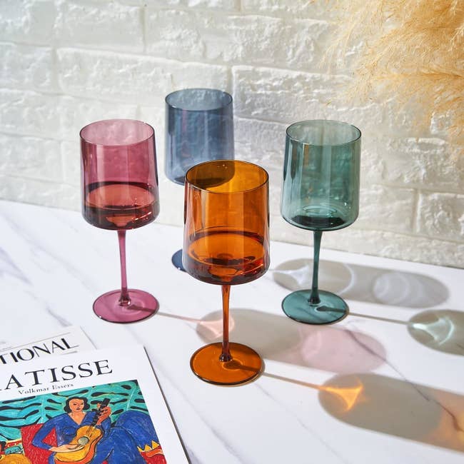 four square wine glasses in deep shades of blue, green, purple, and orange